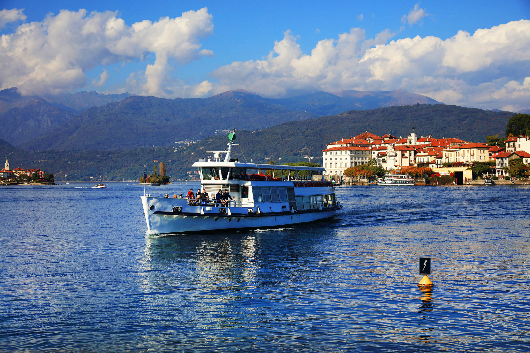 Schiff fährt auf einem See vor einer Stadt mit Bergen im Hintergrund.