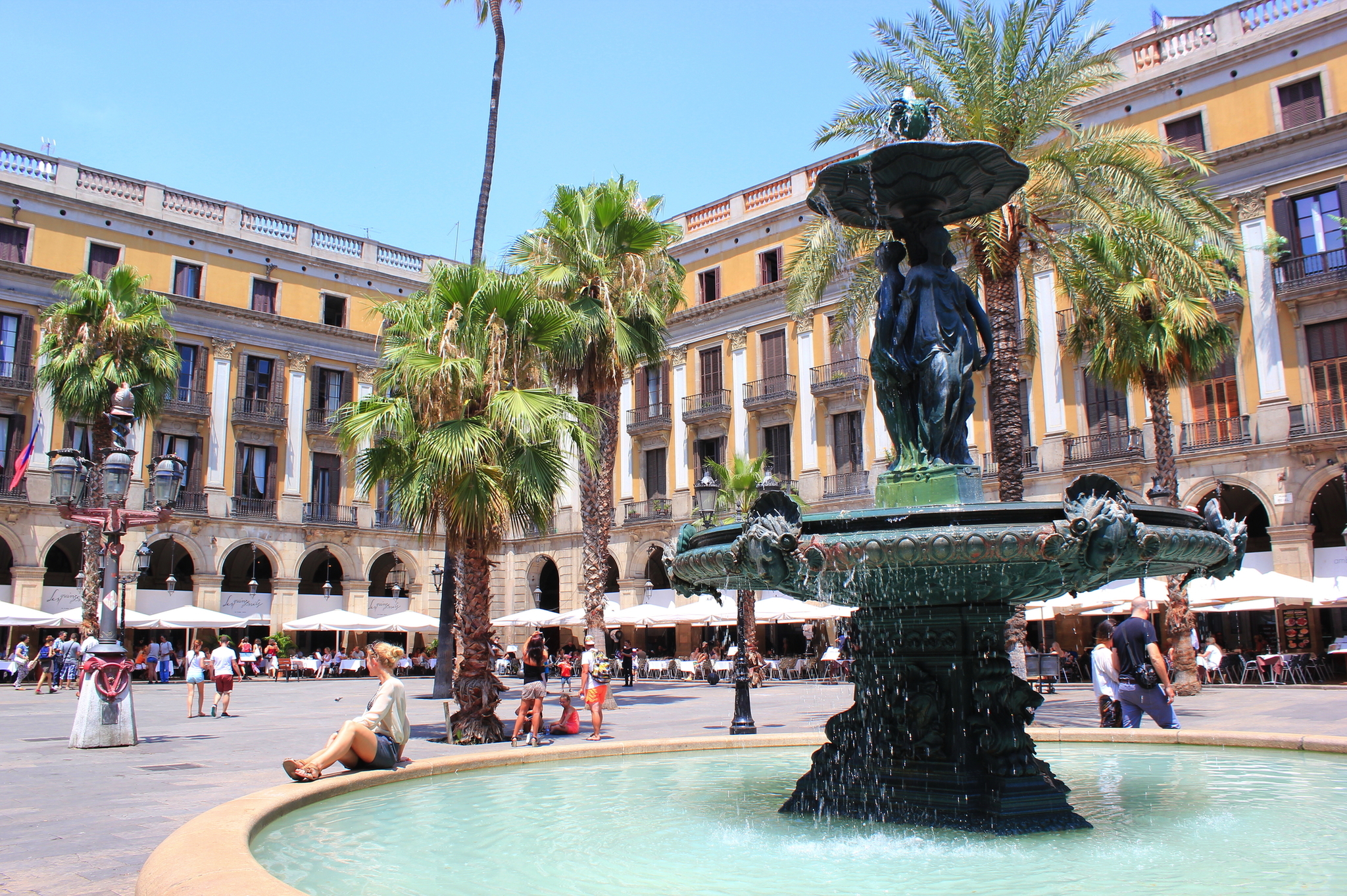Plaça Reial in Barcelona Brunnen auf einem Platz mit Palmen und Menschen im Hintergrund.