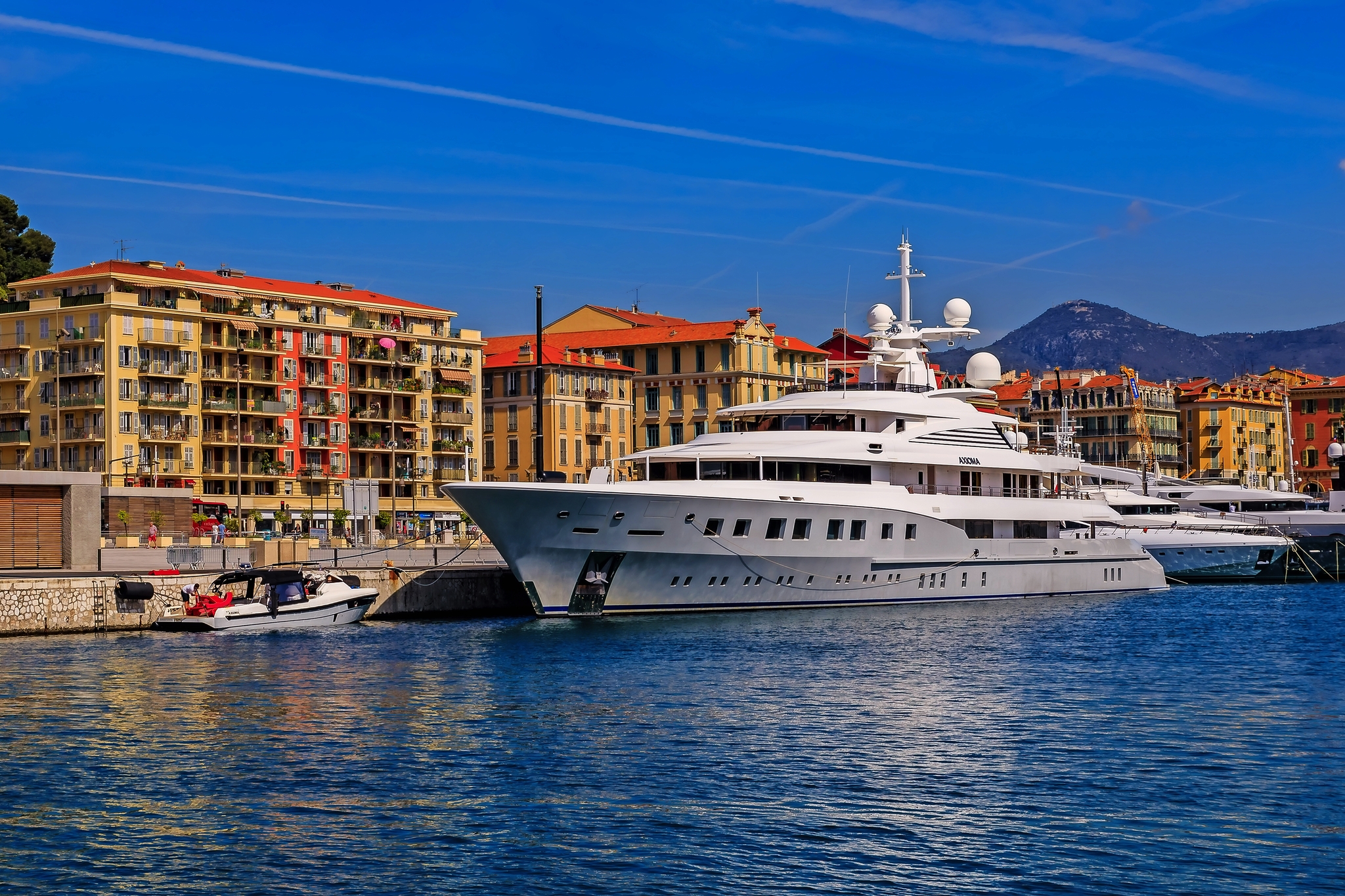 Luxusyacht im Hafen vor einer Stadtkulisse mit Bergen im Hintergrund.