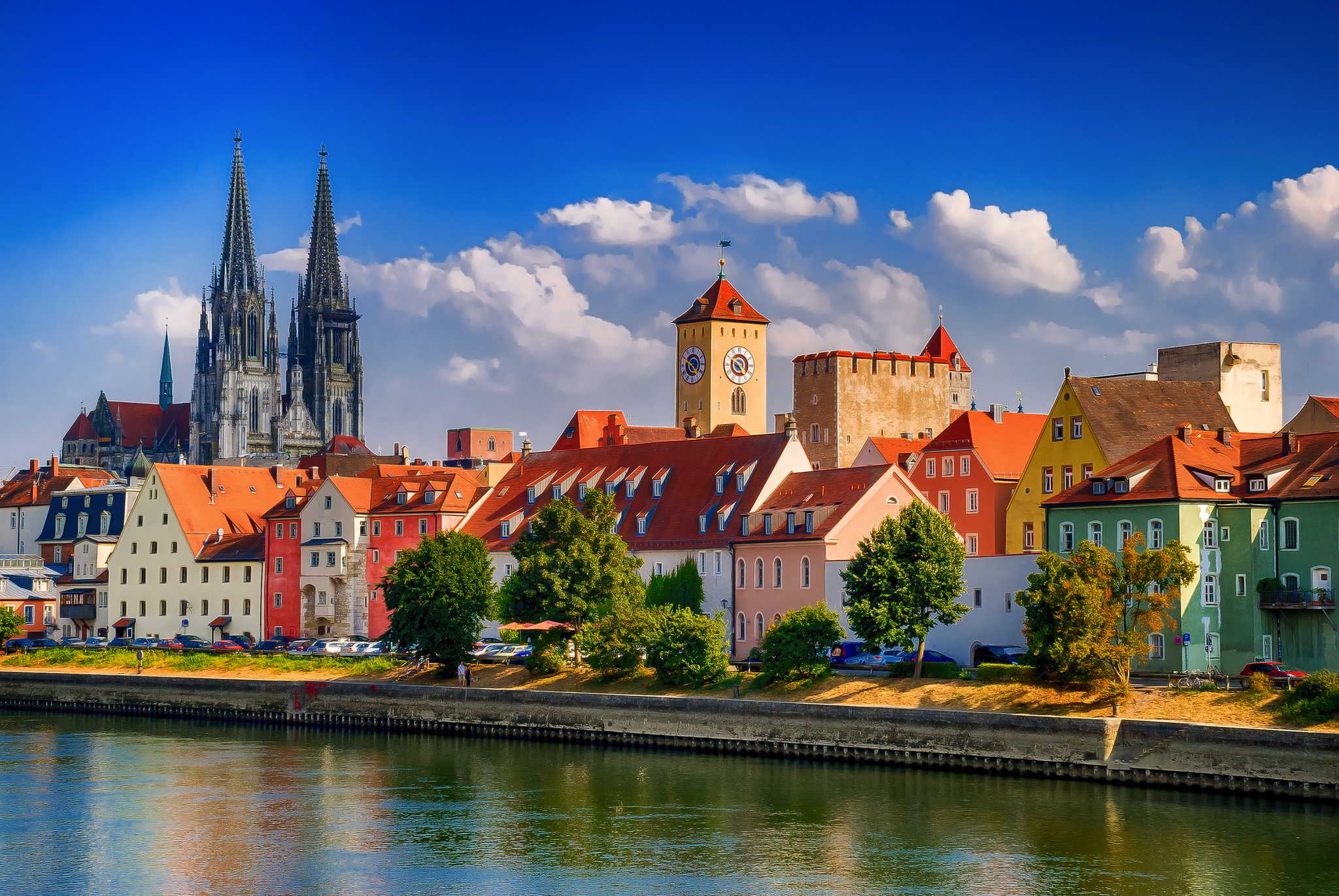 Dom in Regensburg, Deutschland Bunte Häuserzeile am Fluss mit Kathedrale und blauem Himmel im Hintergrund.