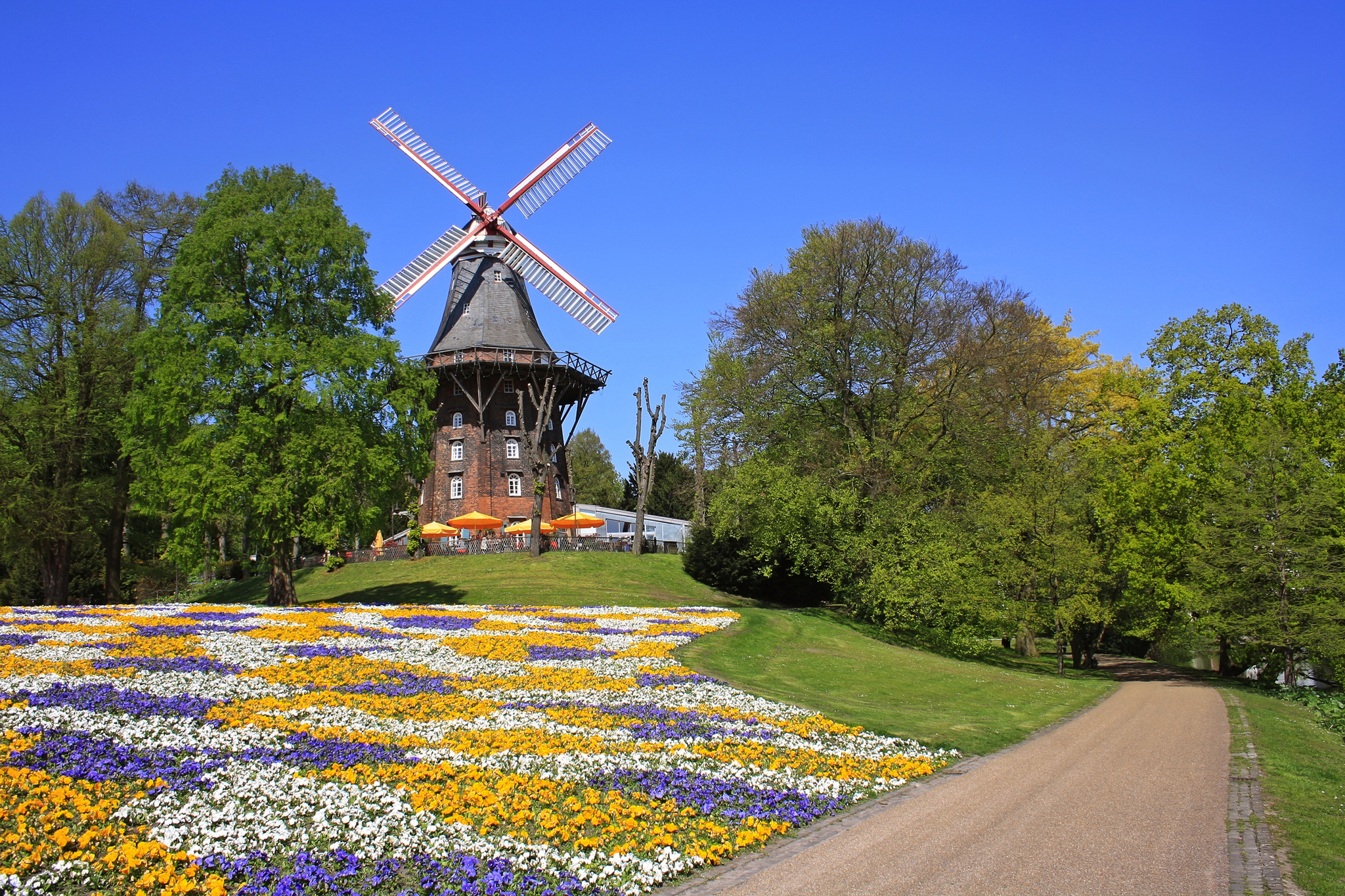 Windmühle in einem Park mit bunten Blumenbeeten im Vordergrund und blauem Himmel im Hintergrund.