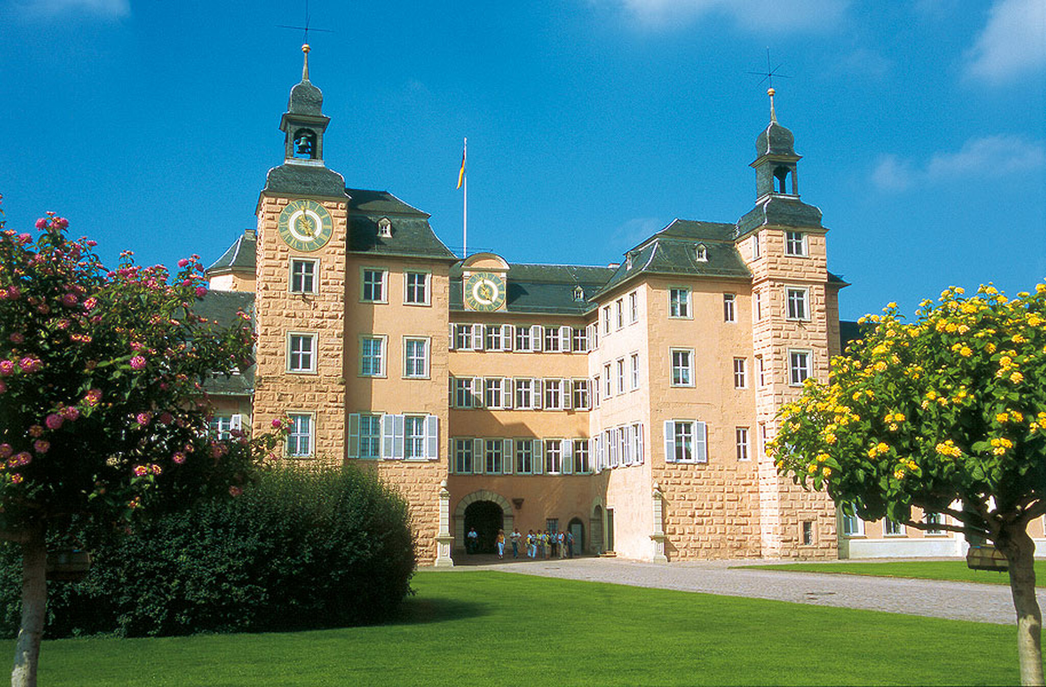 Vorderseite von Schloss Schwetzingen mit Türmen und grünem Rasen im Vordergrund.