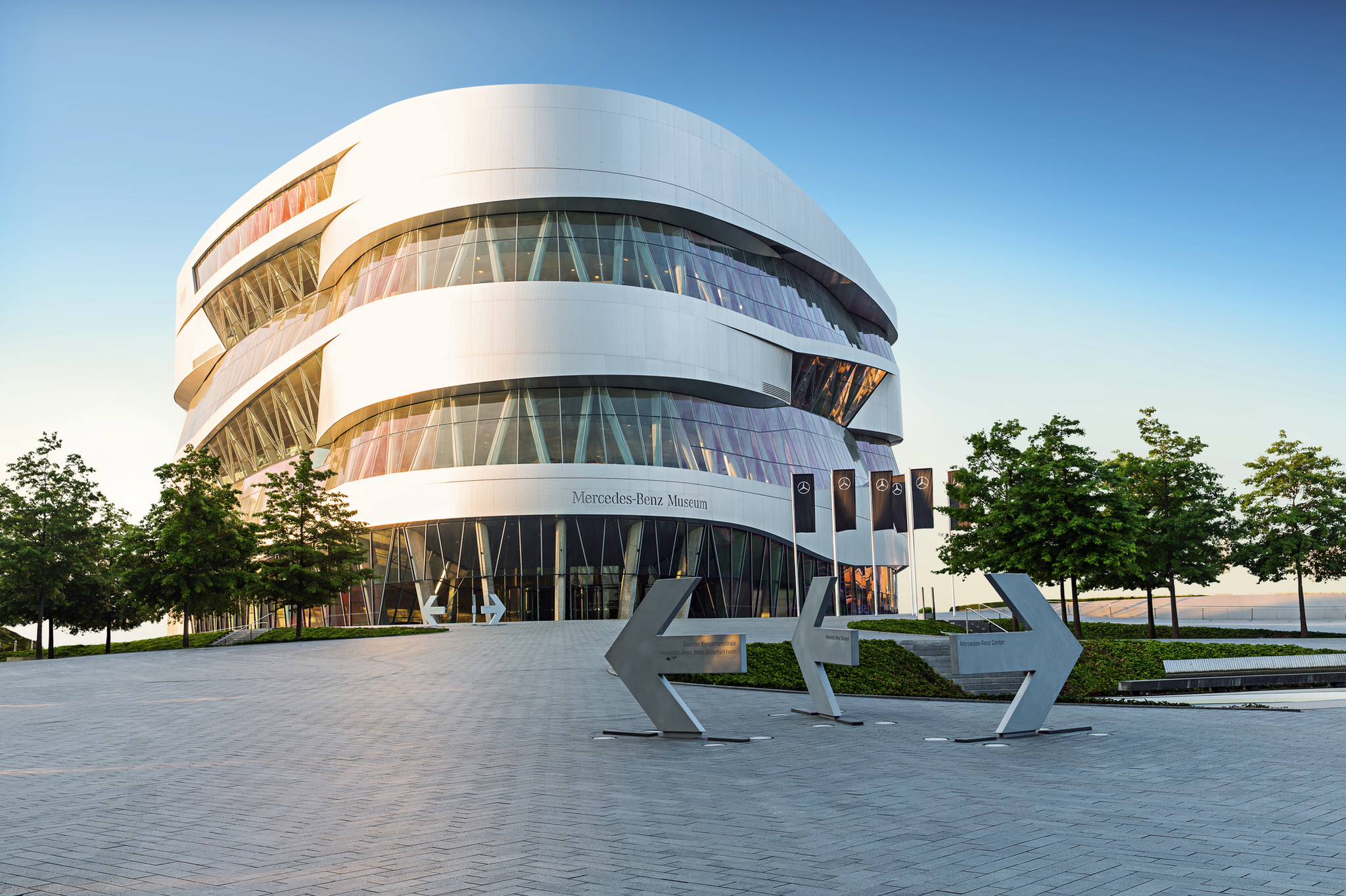 Mercedes-Benz Museum Modernes Gebäude mit Glasfassade und Mercedes-Benz Schriftzug, umgeben von Bäumen.