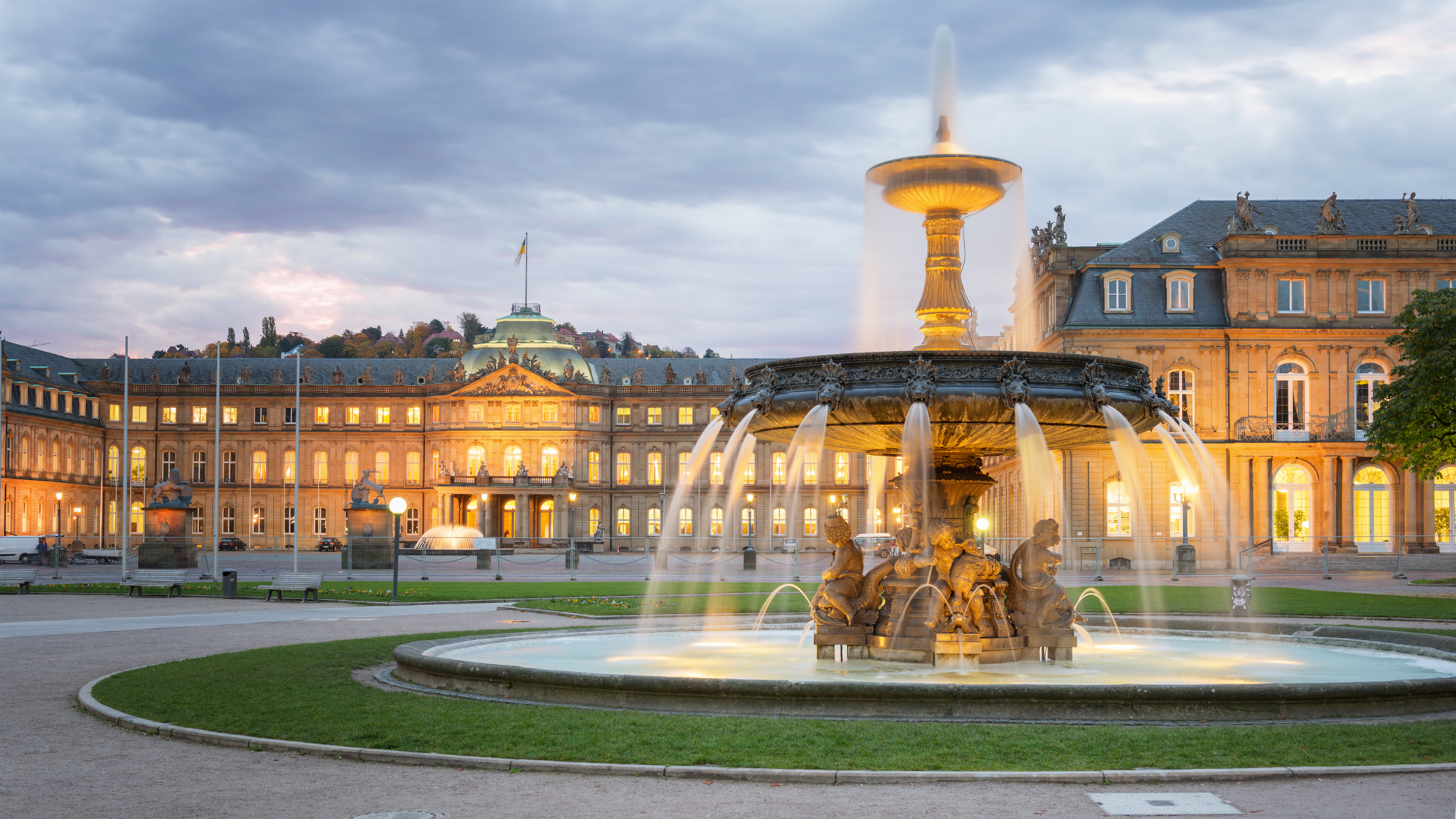 Stuttgarter Schlossplatz, Deutschland Brunnen vor einem beleuchteten Schloss bei bewölktem Himmel.