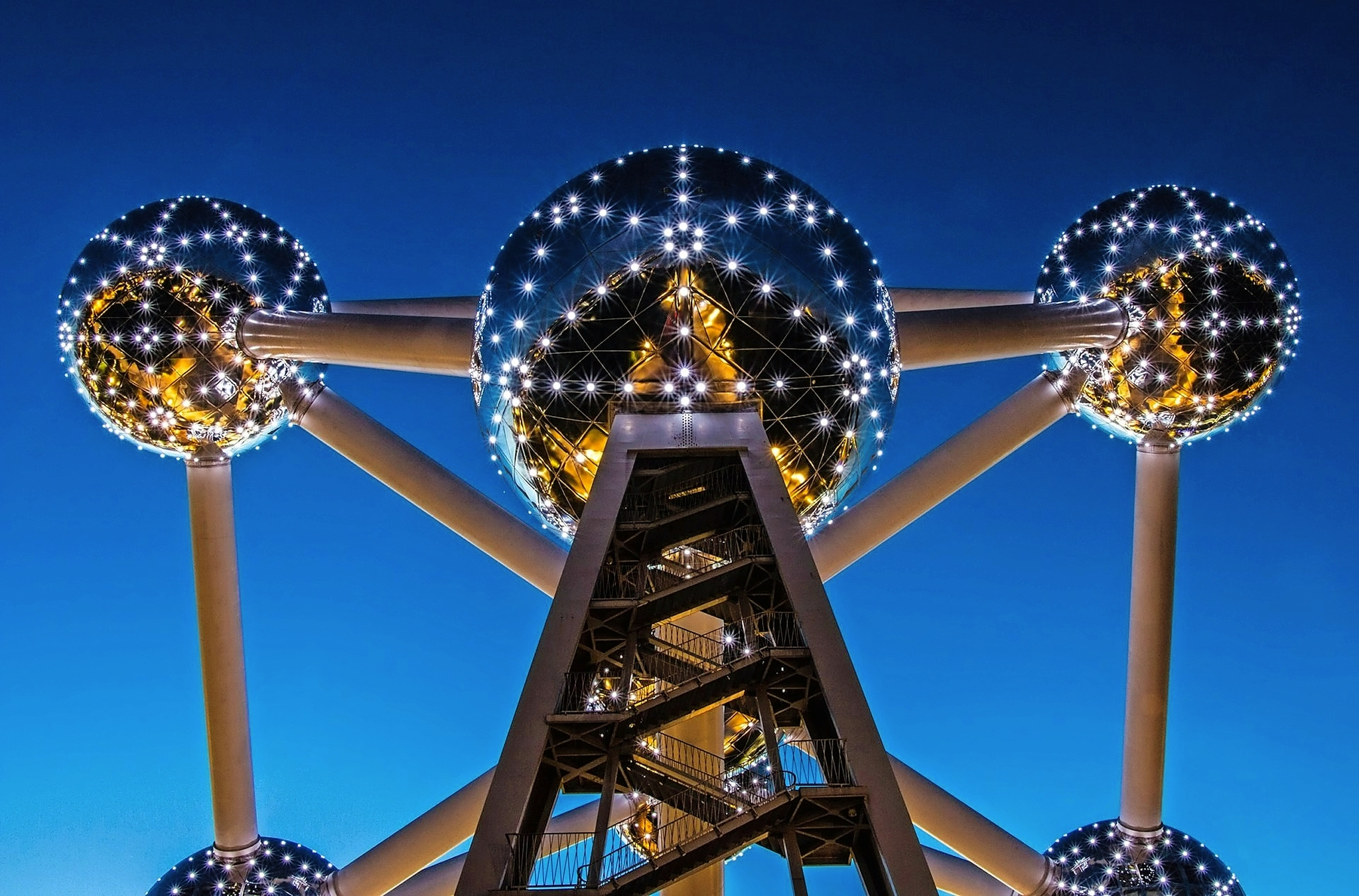 Atomium in Brüssel, Belgien Das Bild zeigt die Struktur des Atomium in Brüssel, Belgien, bei Nacht. Es besteht aus mehreren großen, metallisch glänzenden Kugeln, die durch Röhren verbunden sind, und ist von vielen Lichtern beleuchtet, die in der Dunkelheit funkeln.