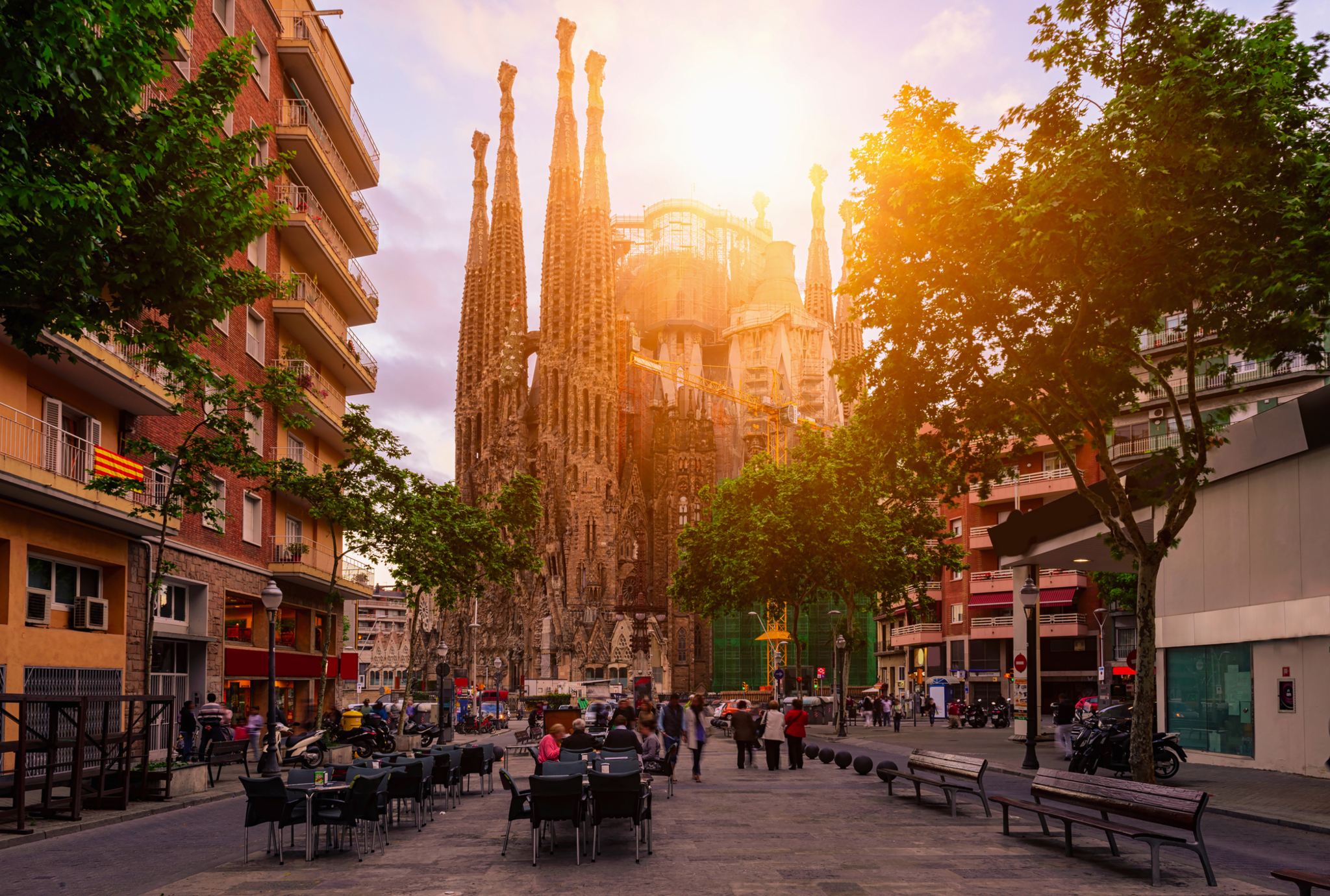 Straßenleben vor der Sagrada Familia in Barcelona Eine belebte Straße mit einer beeindruckenden Kirche im Hintergrund bei Sonnenuntergang.