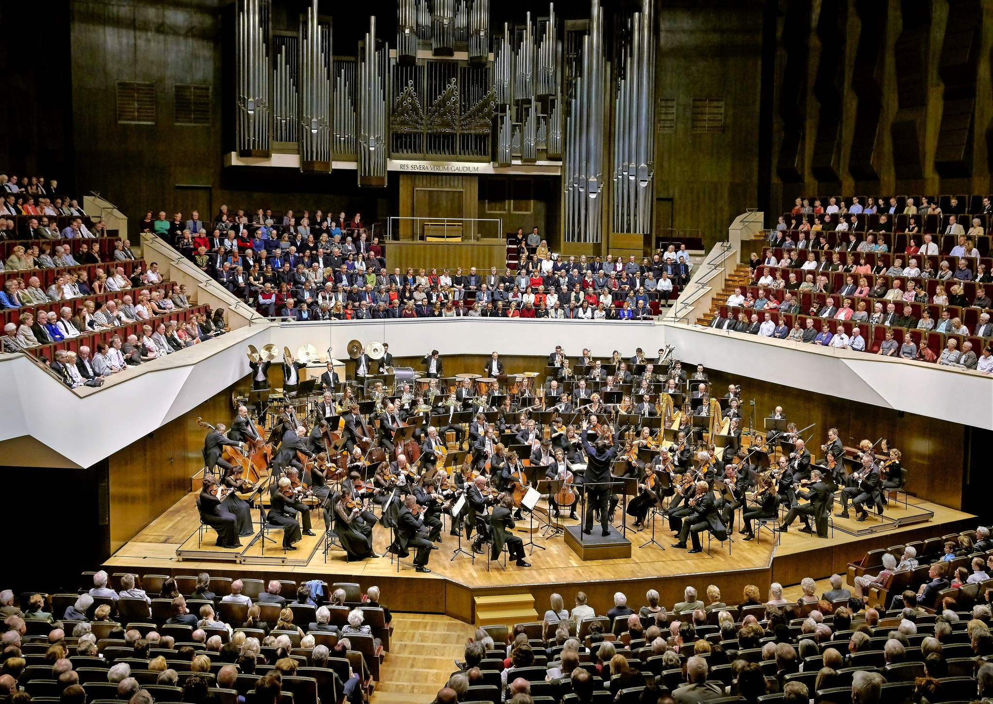 Ein Orchester spielt vor einem großen Publikum in einem Konzertsaal.