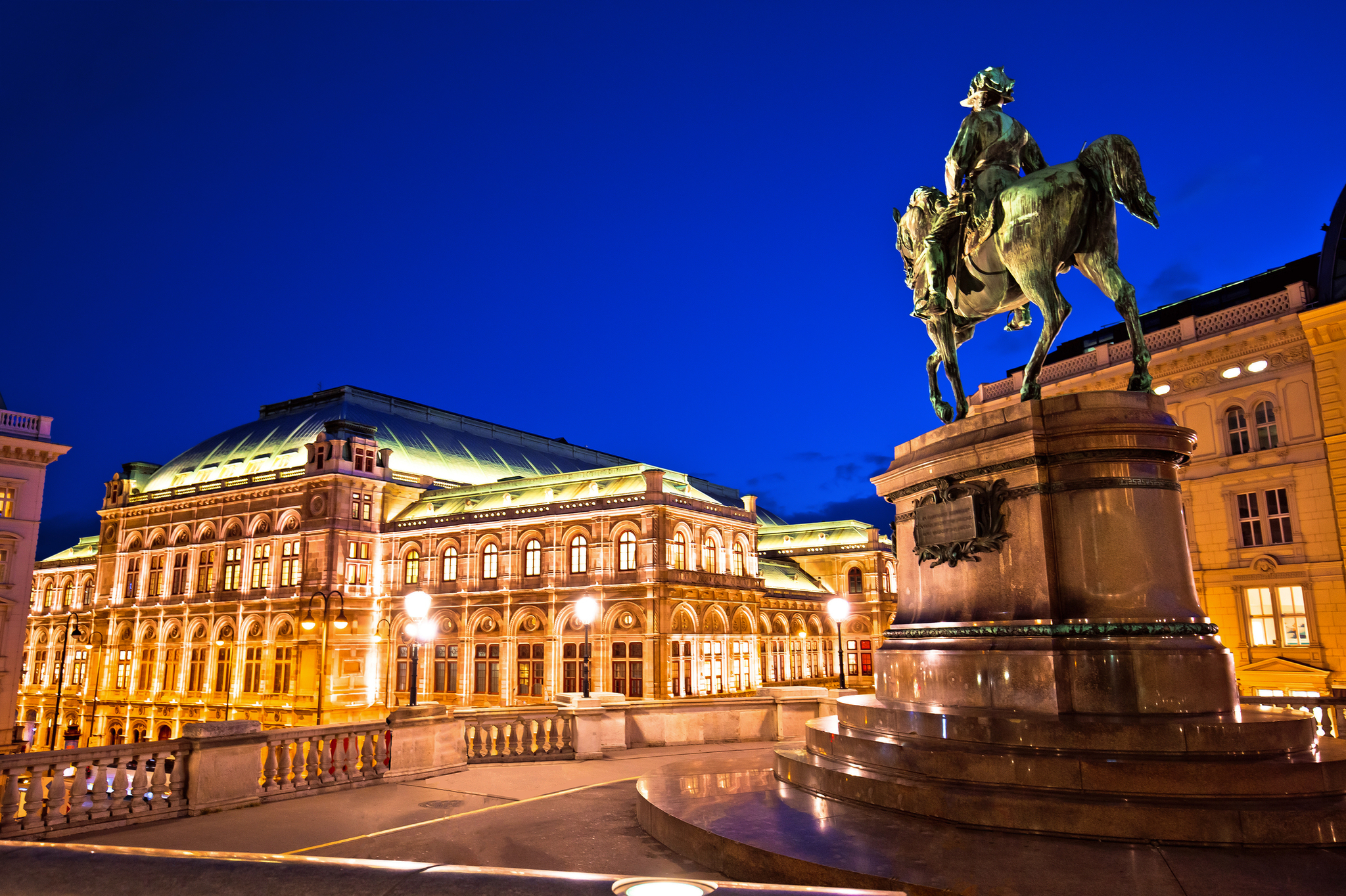 Wiener Staatsoper Reiterstatue im Vordergrund mit einem großen, beleuchteten Gebäude im Hintergrund bei Nacht.