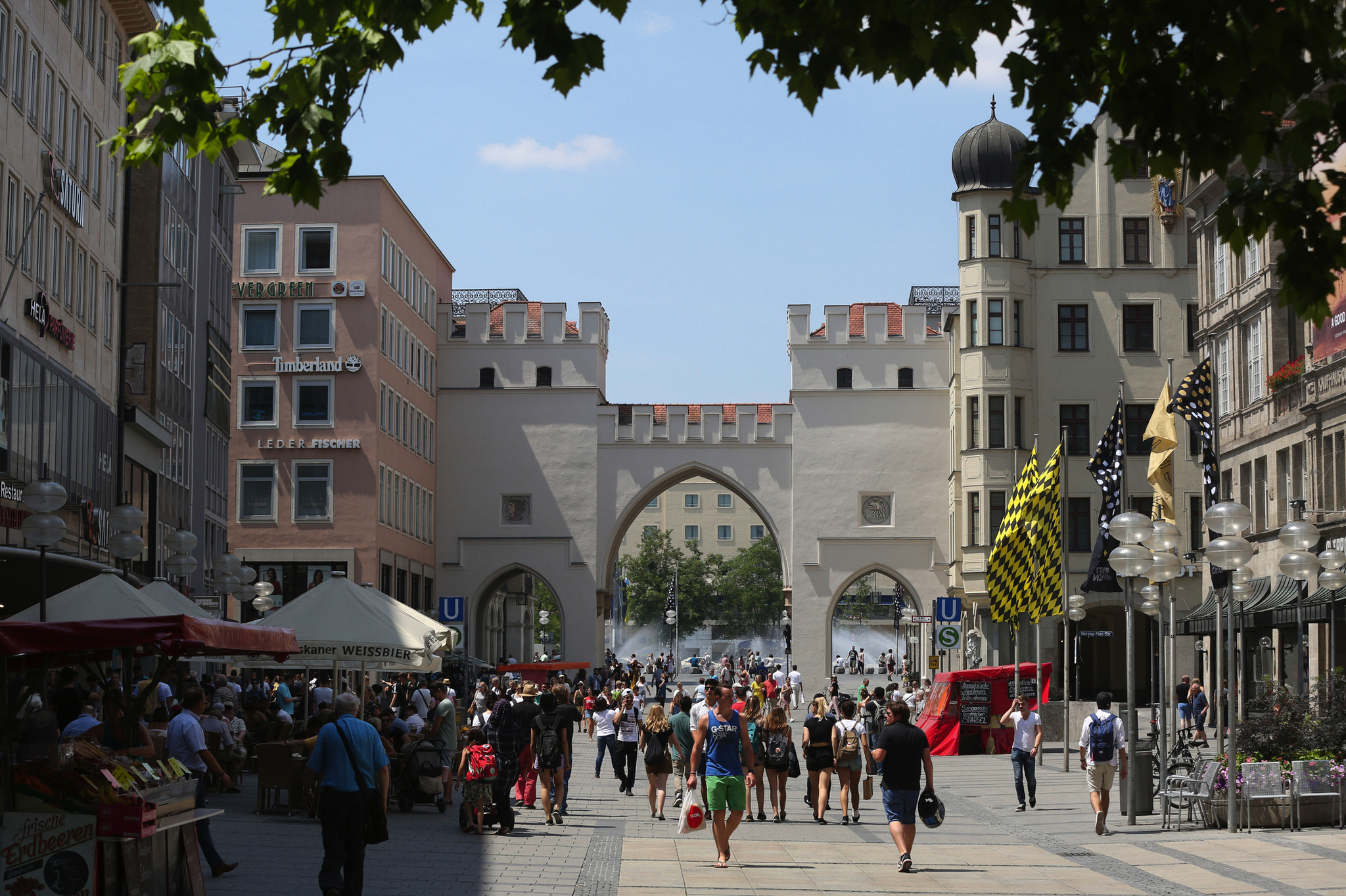 Das Karlstor in München im Sommer mit vielen Passanten und blühender Umgebung.