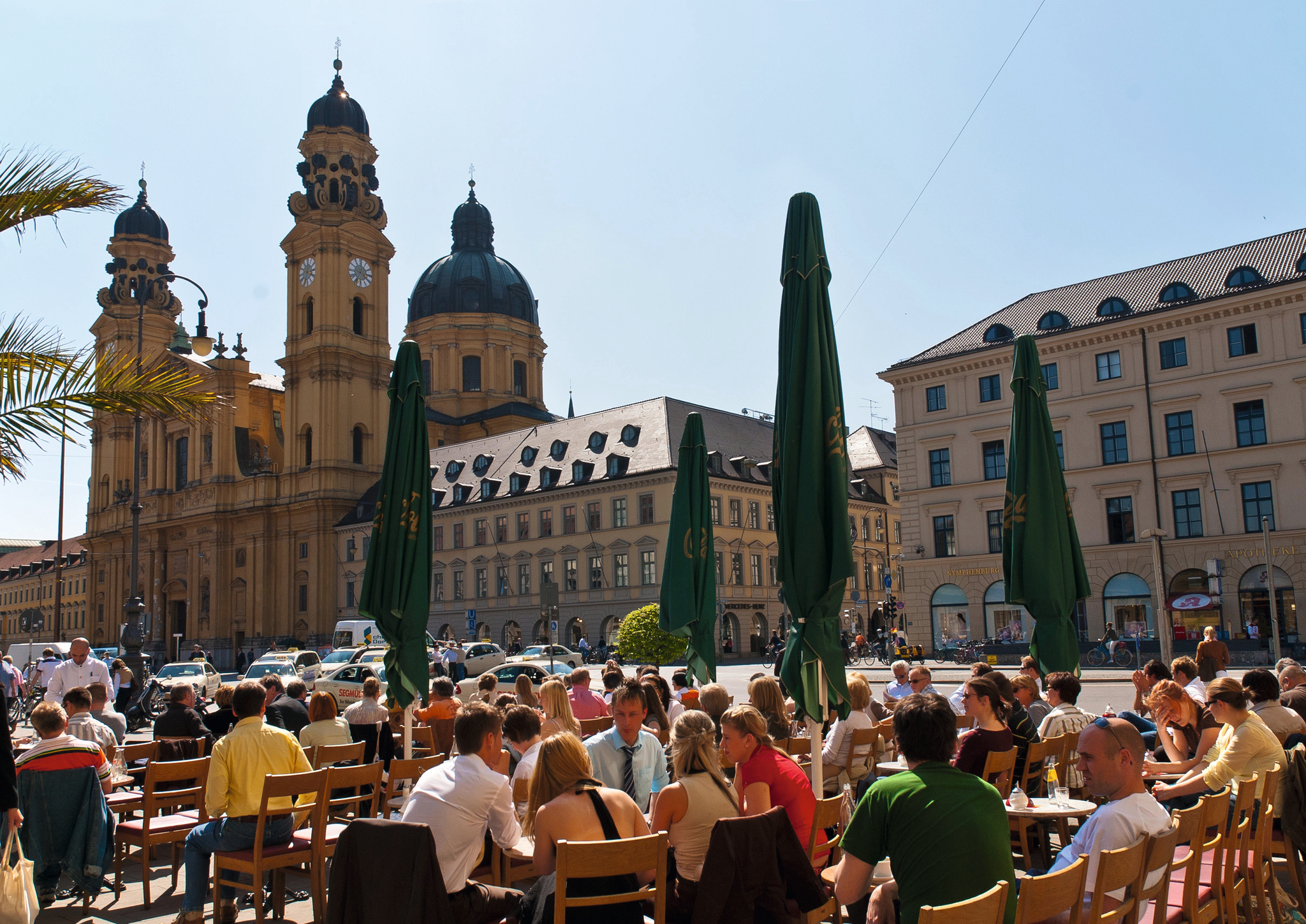 Menschen sitzen draußen im Café am Odeonsplatz in München bei sonnigem Wetter.