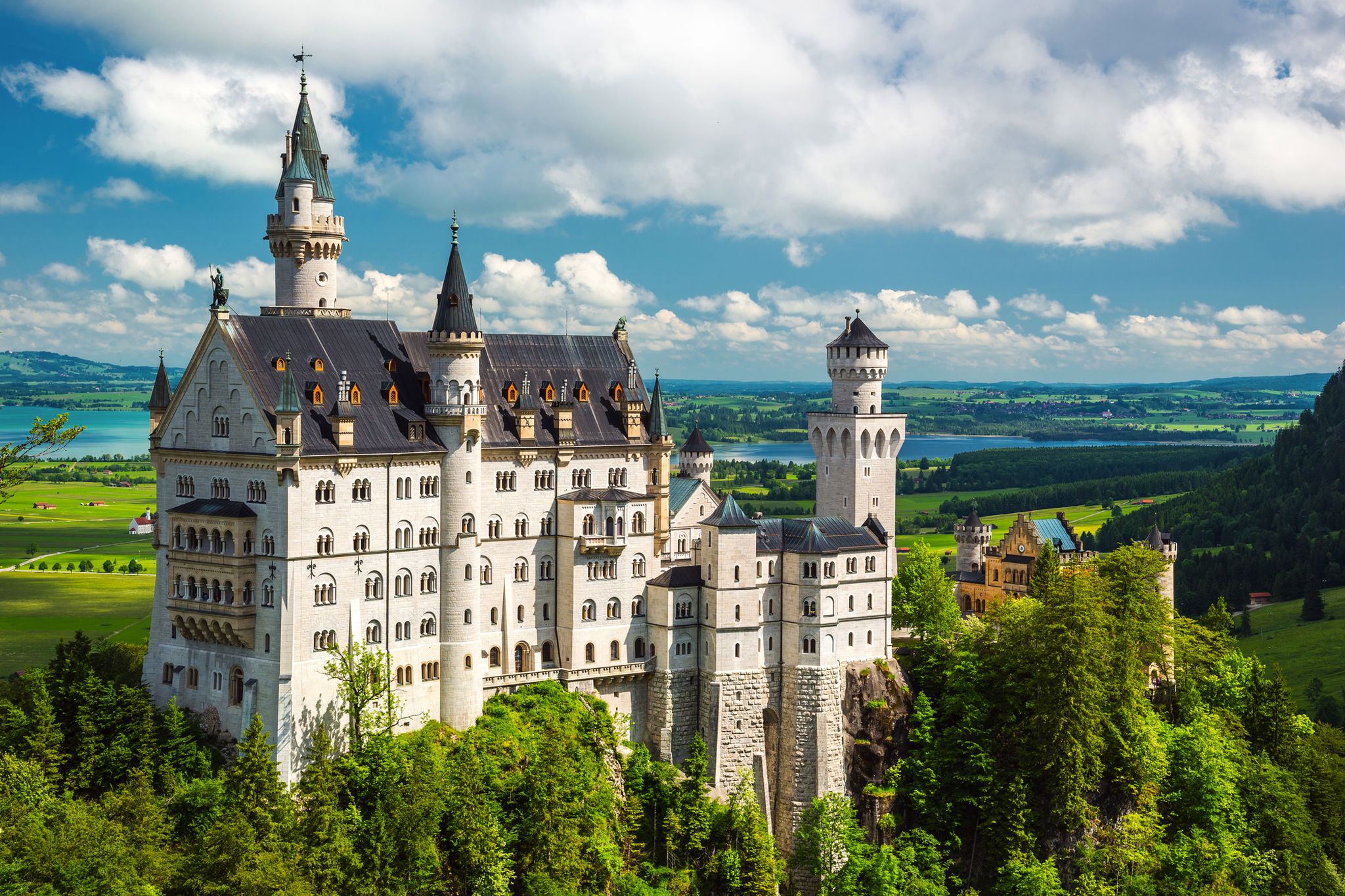 Schloss Neuschwanstein vor Alpenkulisse mit blauem Himmel und Wolken.