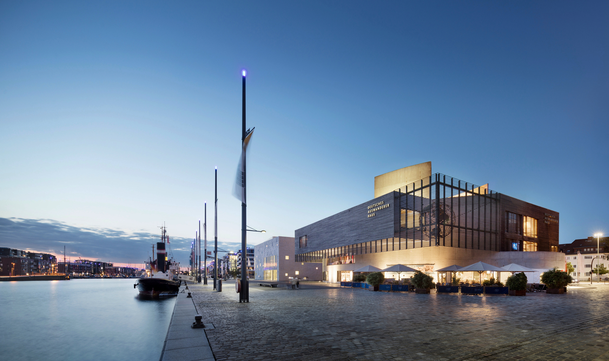 Deutsches Auswandererhaus bei Dämmerung am Hafen mit Wasser und Booten.