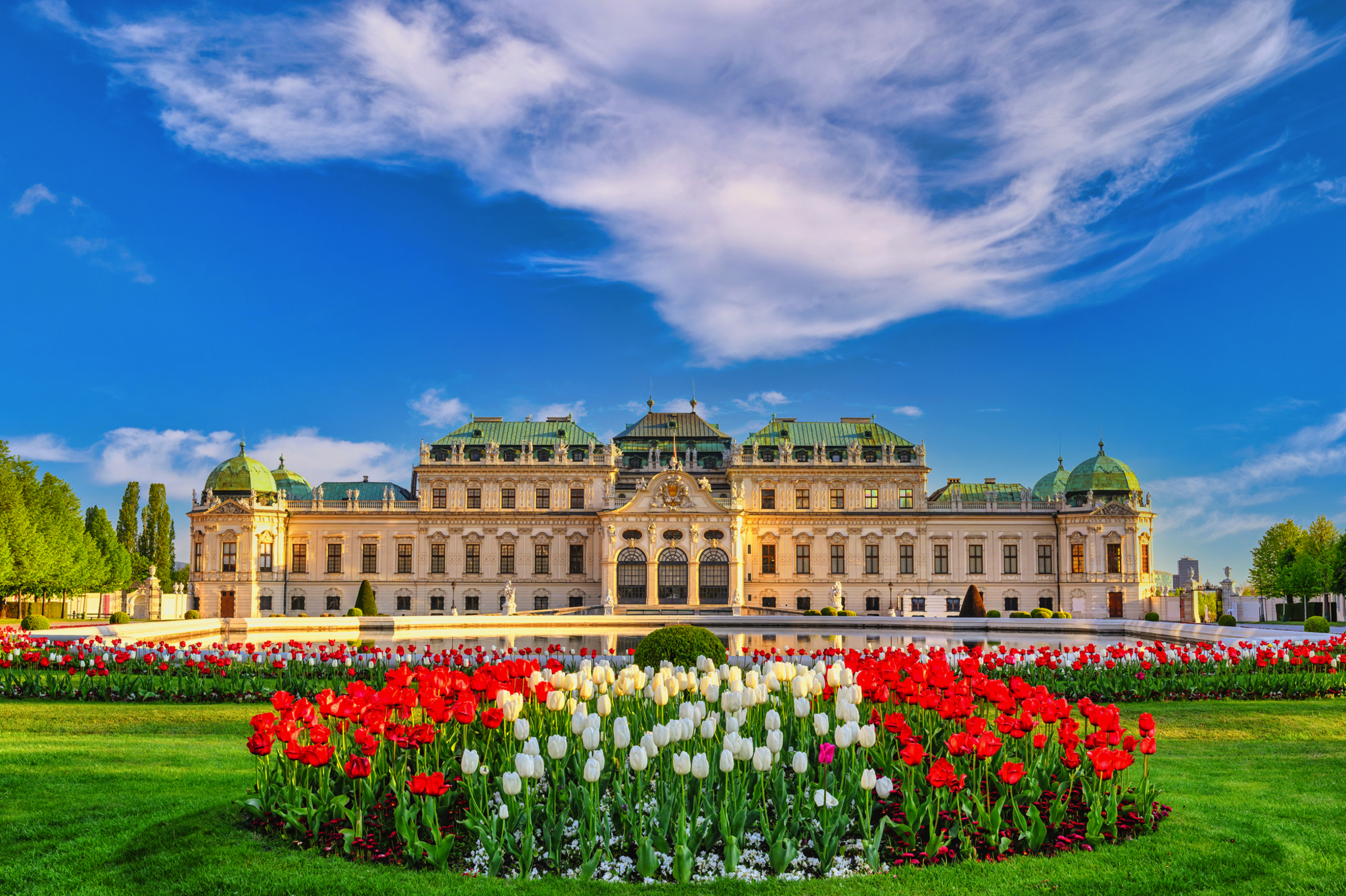 Schloss Belvedere in Wien, Österreich Barockes Schloss mit Blumenbeeten im Vordergrund und blauem Himmel.