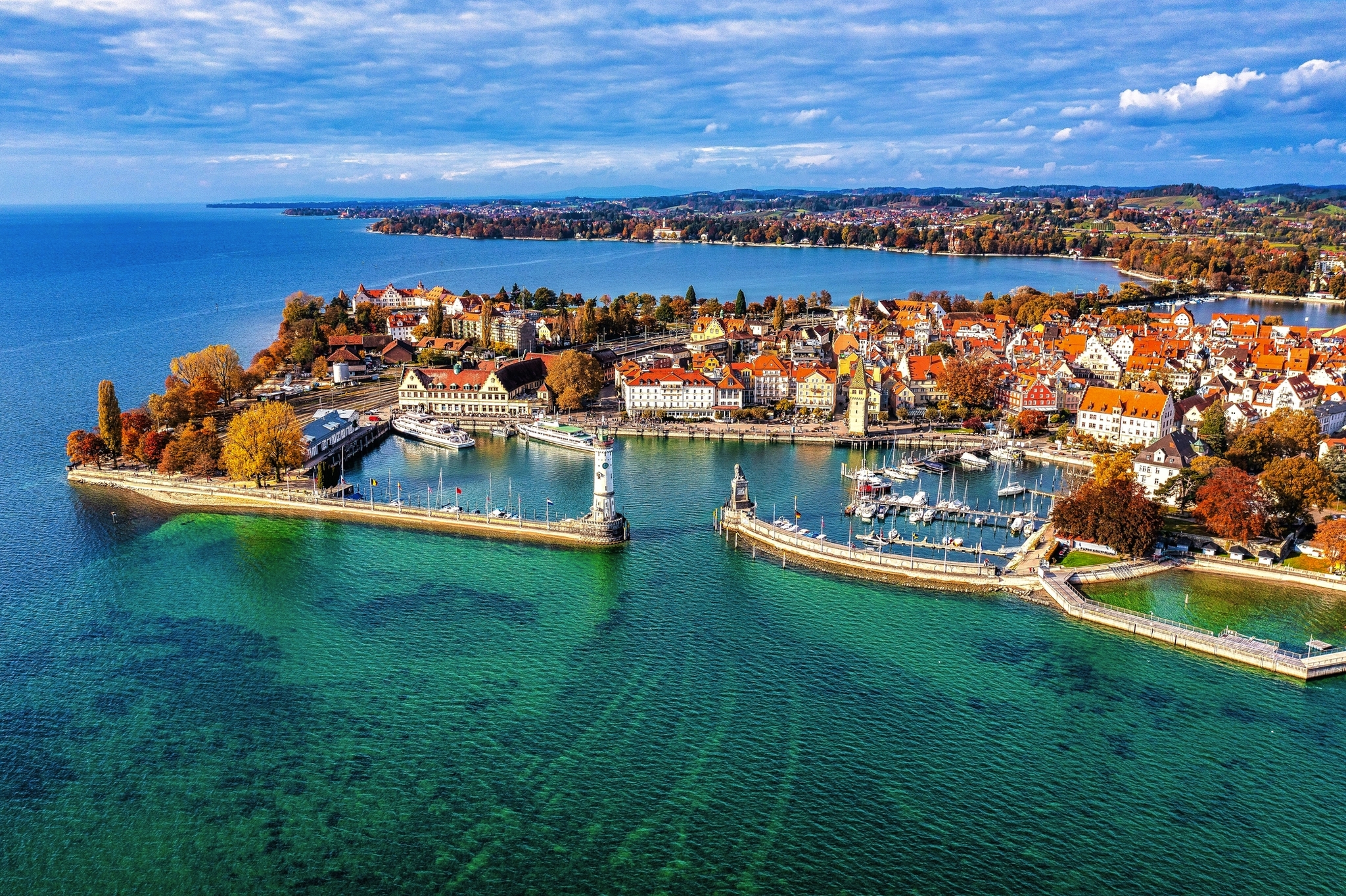 Urlaub am Bodensee Luftaufnahme einer Hafenstadt mit Seen und herbstlichen Bäumen.