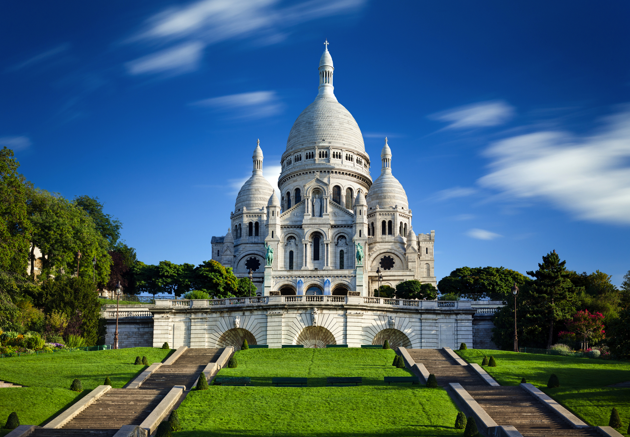 Basilika Sacré-Cœur in Paris vor blauem Himmel und üppigem grünen Park.