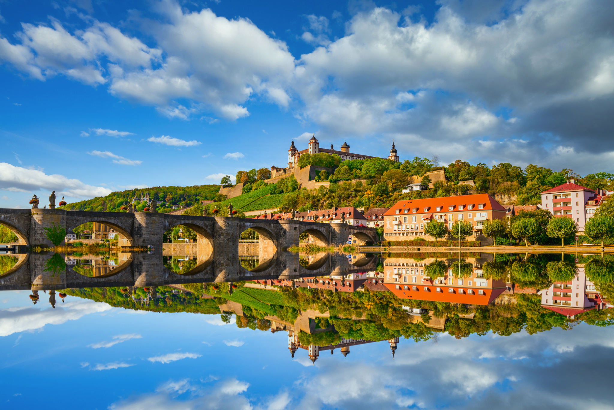 Brücke über Fluss mit Schloss und bewölktem Himmel im Hintergrund.