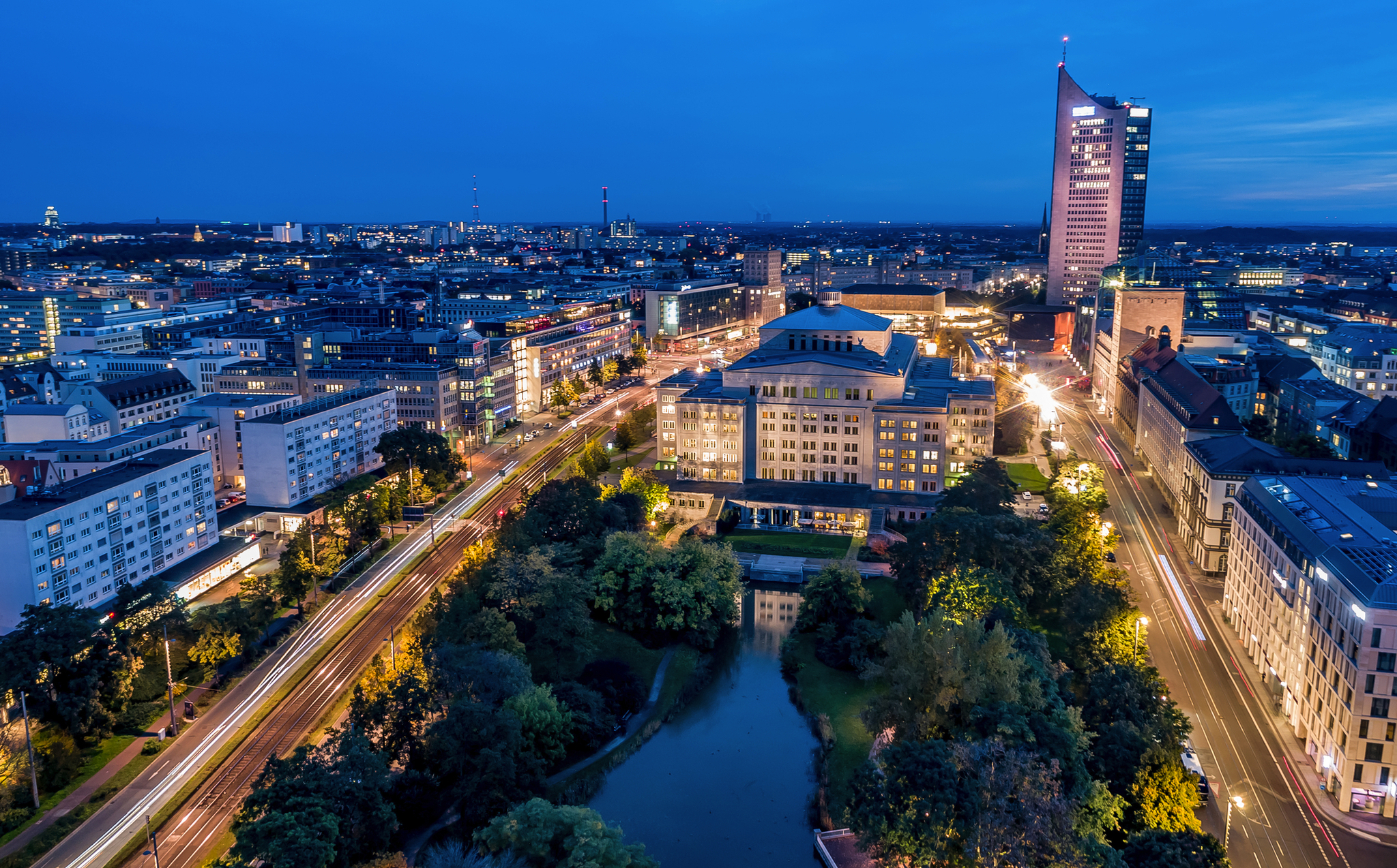 Schwanenteich von Leipzig Stadtansicht von Leipzig bei Dämmerung mit beleuchteten Straßen und hohen Gebäuden.