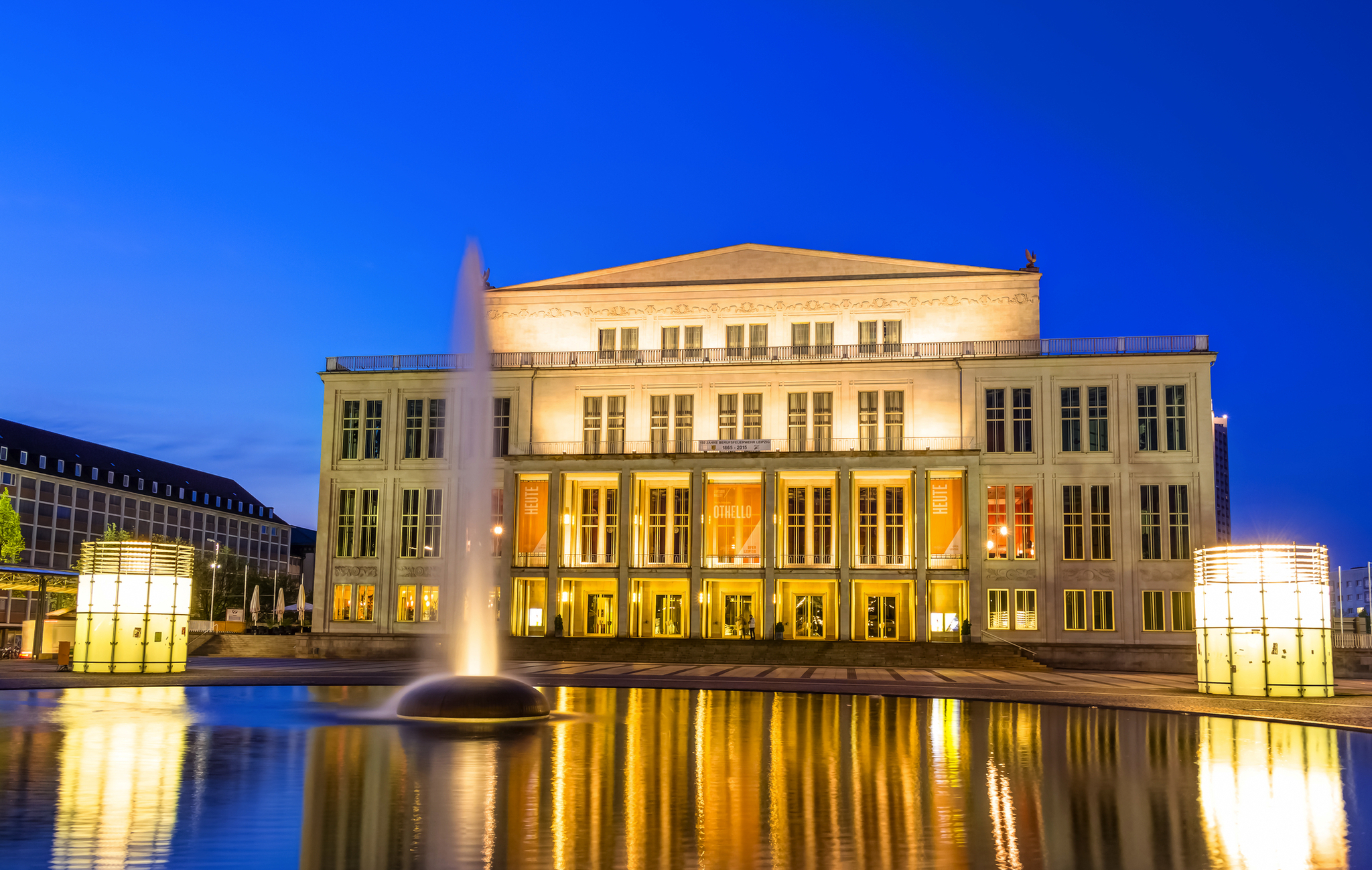 Opernhaus am Abend mit Beleuchtung und reflektierendem Wasser im Vordergrund.