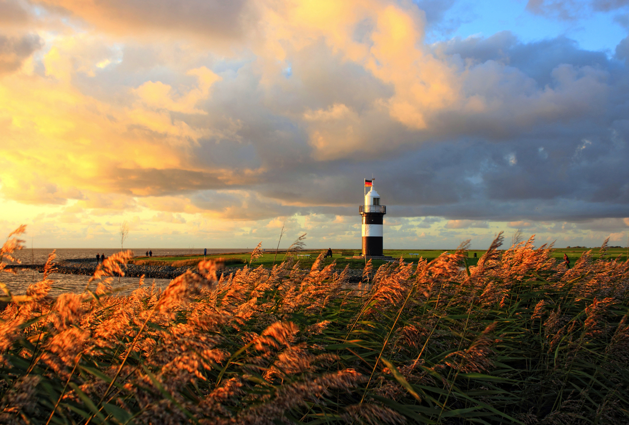 Leuchtturm bei Sonnenuntergang hinter grasbewachsener Küstenlandschaft.