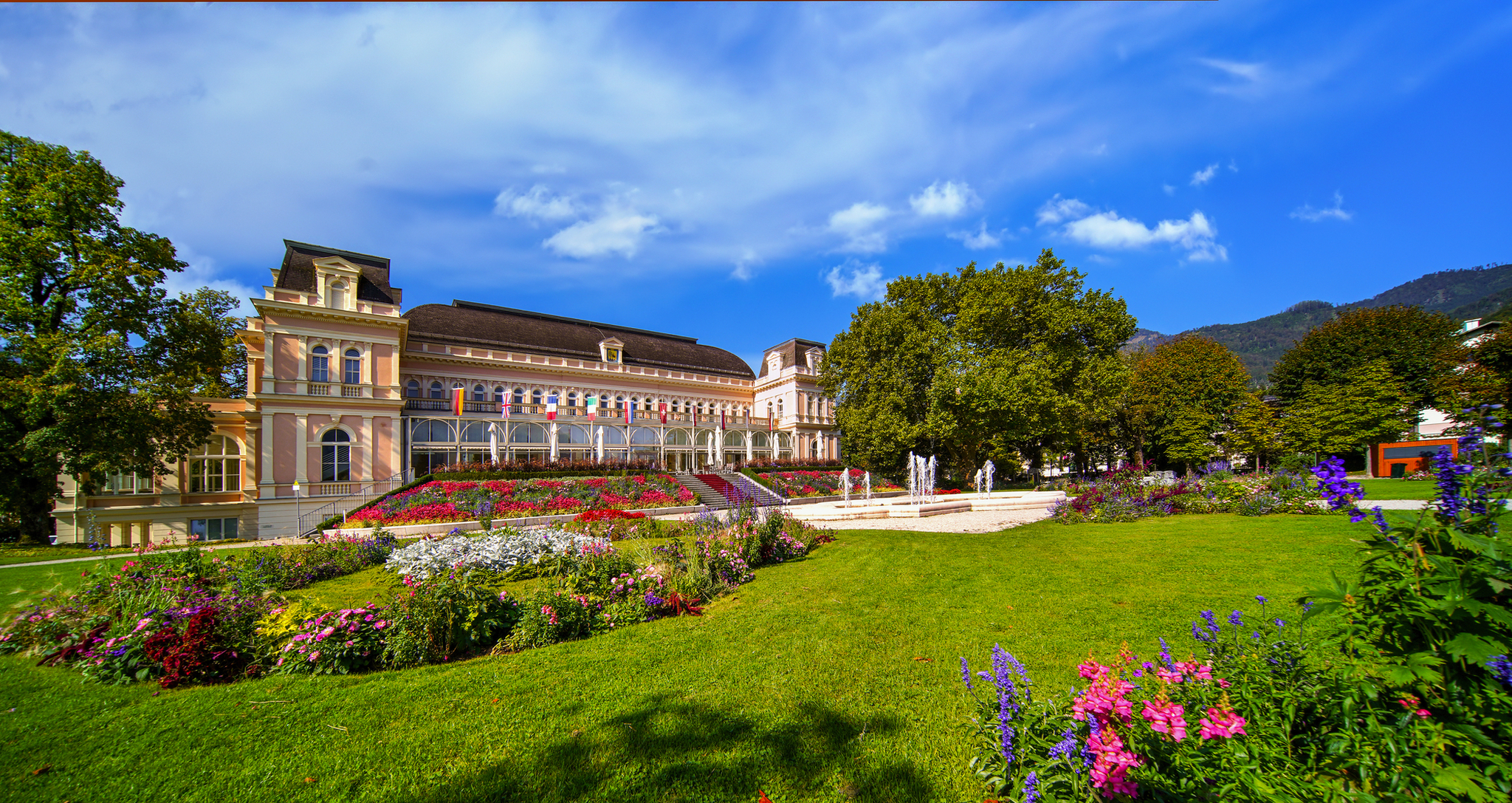 Historisches Gebäude mit Garten, bunten Blumen und Bäumen unter blauem Himmel.
