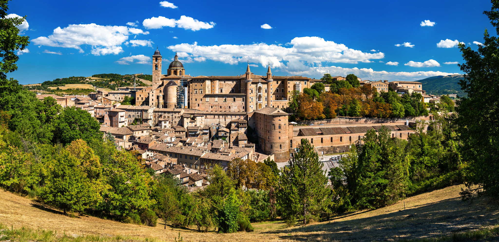 Stadtbild von Urbino in der Region Marken, Italien, mit malerischen Gebäuden und grüner Umgebung.