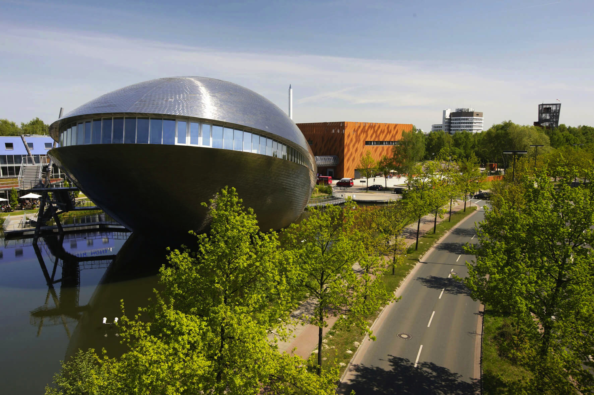 Science Center mit ovalem Gebäude und Turm, von Straße aus gesehen, umgeben von Bäumen.