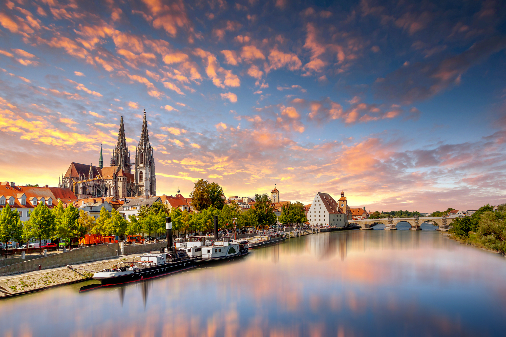 Dom zu Regensburg Städtische Flusslandschaft mit Kirche und Brücke im Sonnenuntergang.