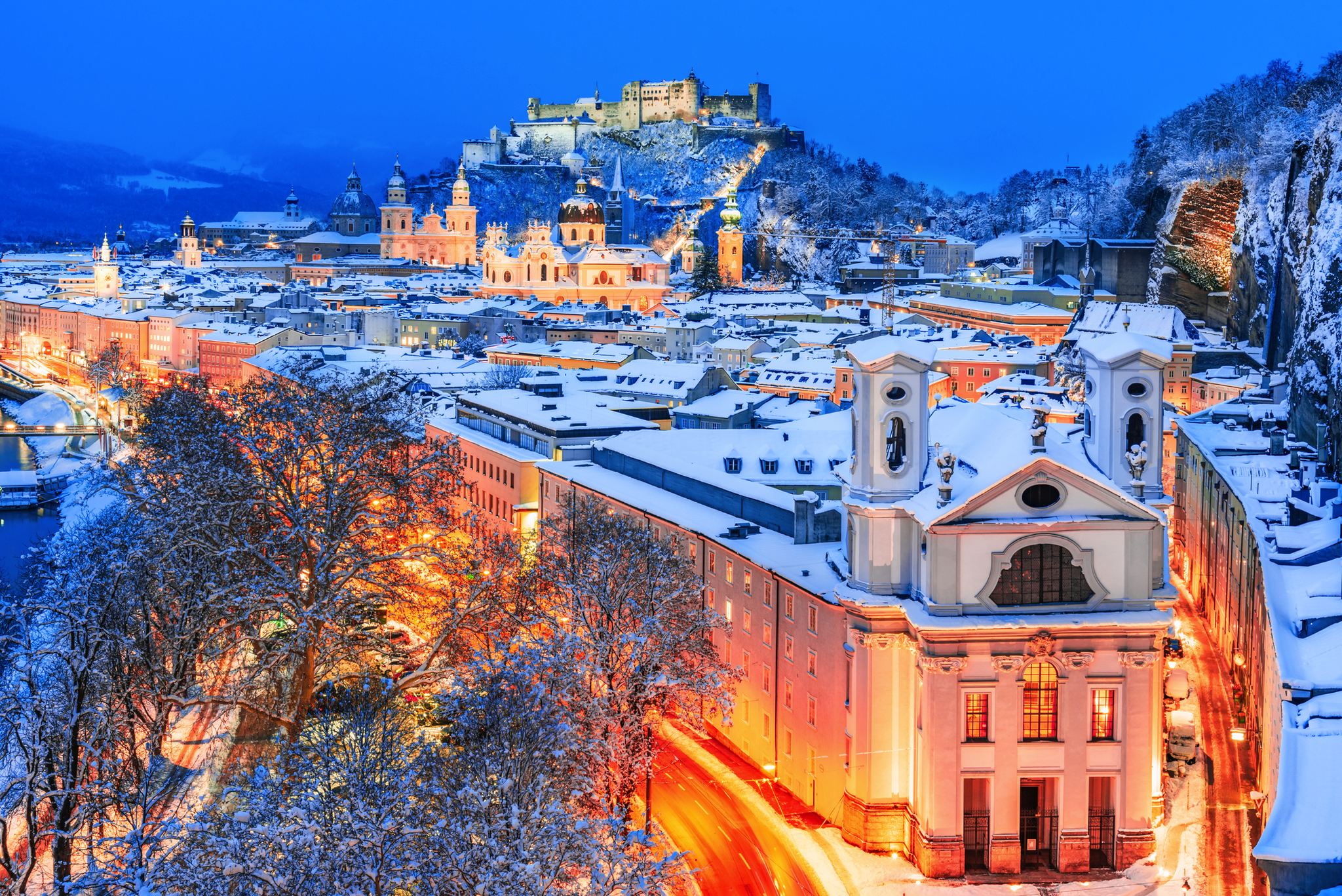 Winteransicht der historischen Stadt Salzburg mit der berühmten Festung Hohensalzburg Verschneite Stadtansicht mit Festung im Hintergrund bei Nacht.