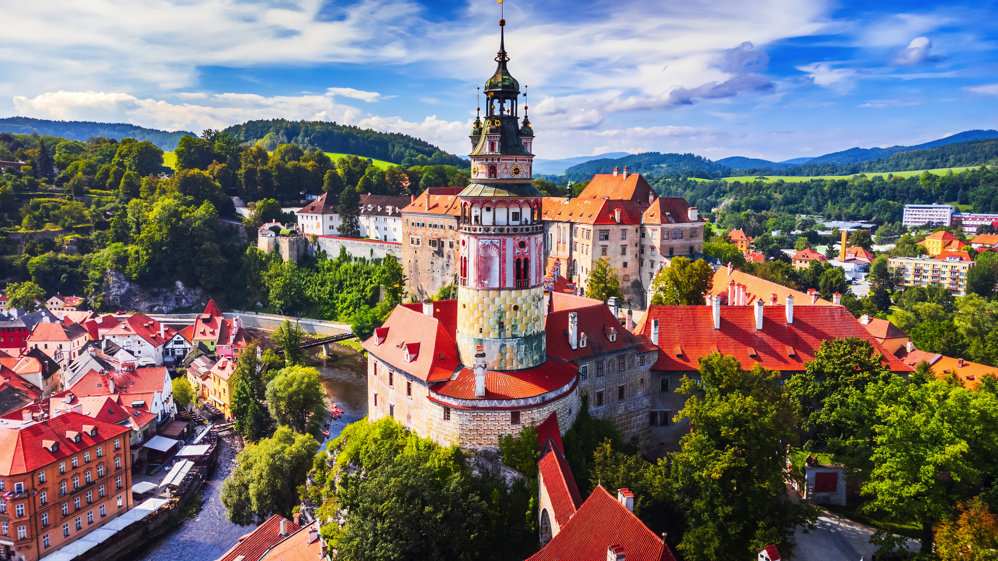 Luftaufnahme einer malerischen Burg mit roten Dächern und umliegender Landschaft.