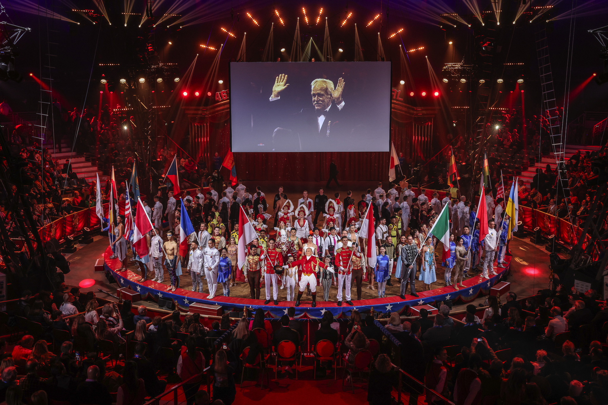 Zirkusfestival in Monte Carlo Eine Bühne voller Menschen mit nationalen Flaggen unter einem großen Bildschirm.