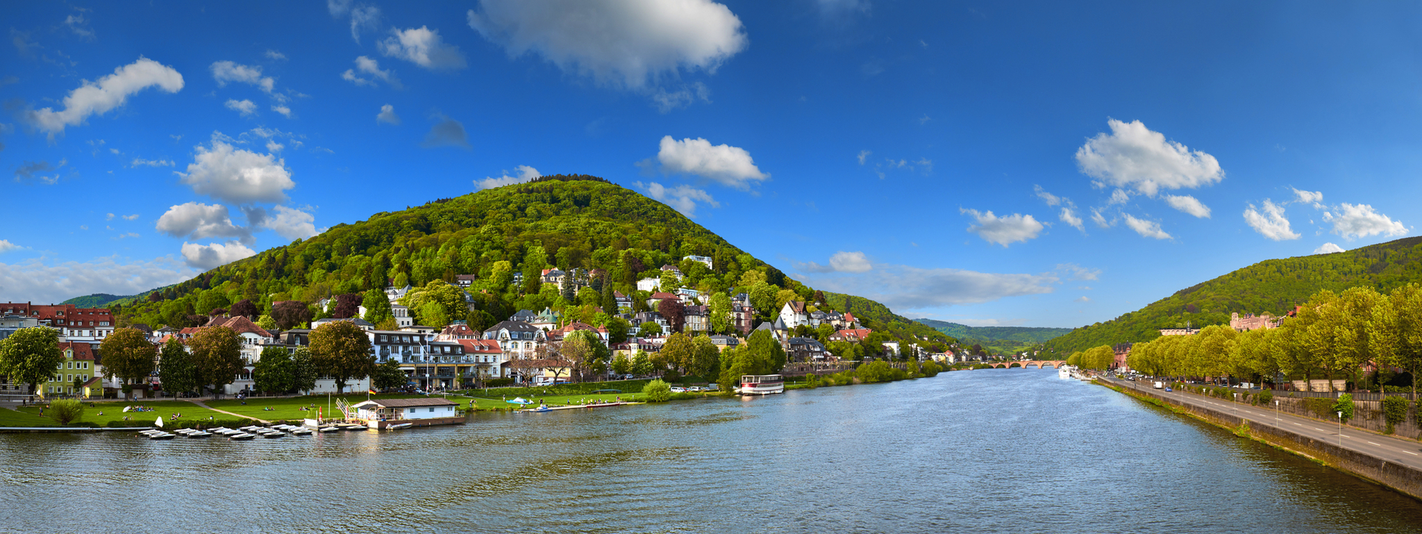 Panoramablick auf Heidelberg und den Neckar von der Karl-Theodor-Brücke Panoramablick auf die Stadt Heidelberg in Baden-Württemberg mit dem Fluss Neckar, gesehen von der Karl-Theodor-Brücke. Im Hintergrund sind grüne Hügel zu sehen.
