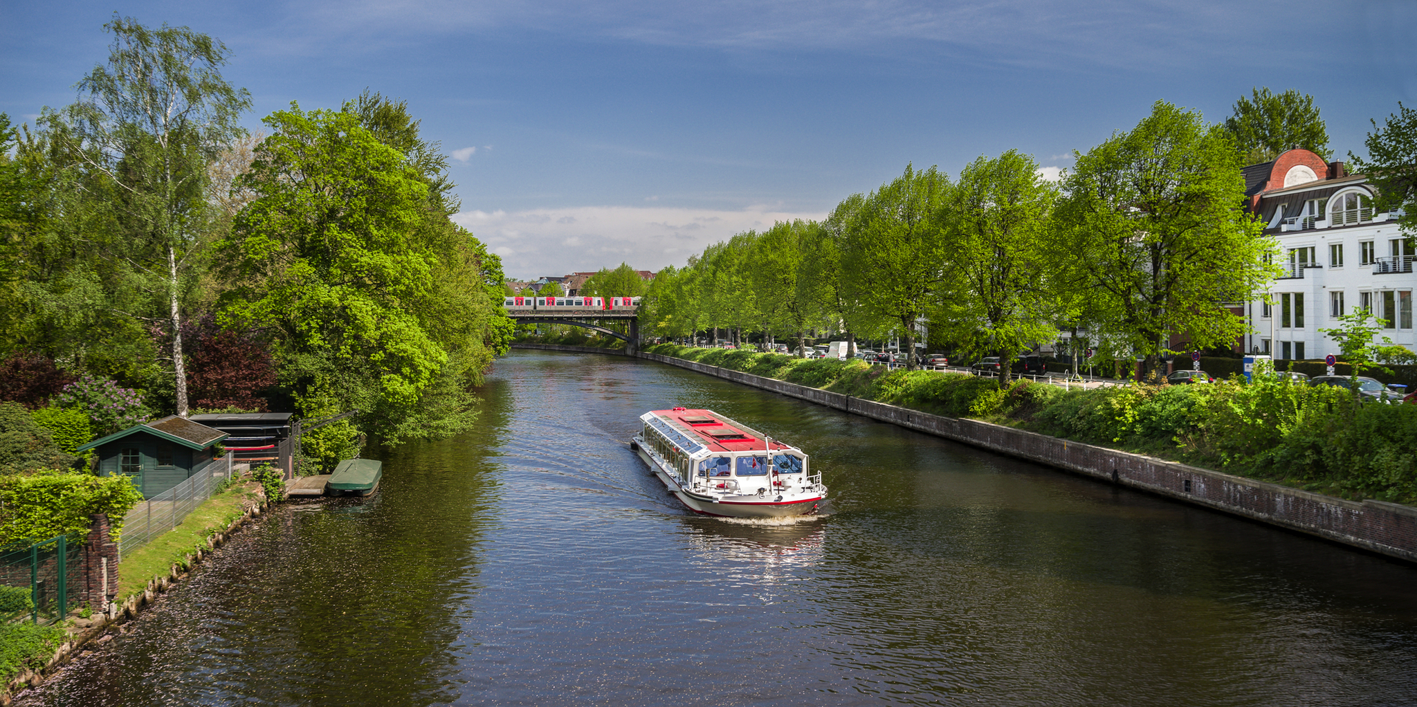 Boot fährt auf einem von Bäumen gesäumten Kanal unter blauem Himmel.
