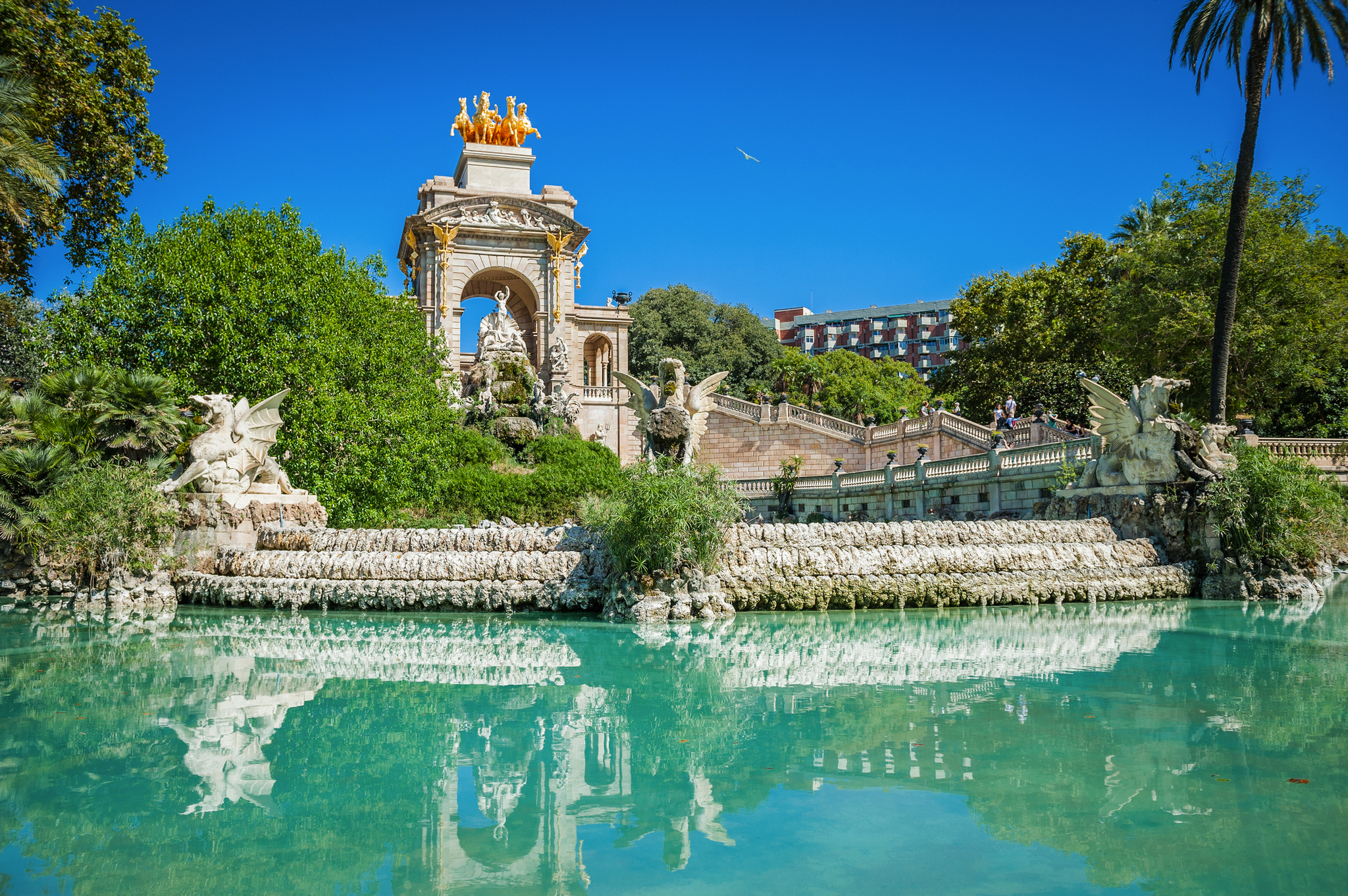 Brunnenpark Ciutadella in Barcelona Springbrunnen und Statue in einem Park vor blauem Himmel und Palmen.