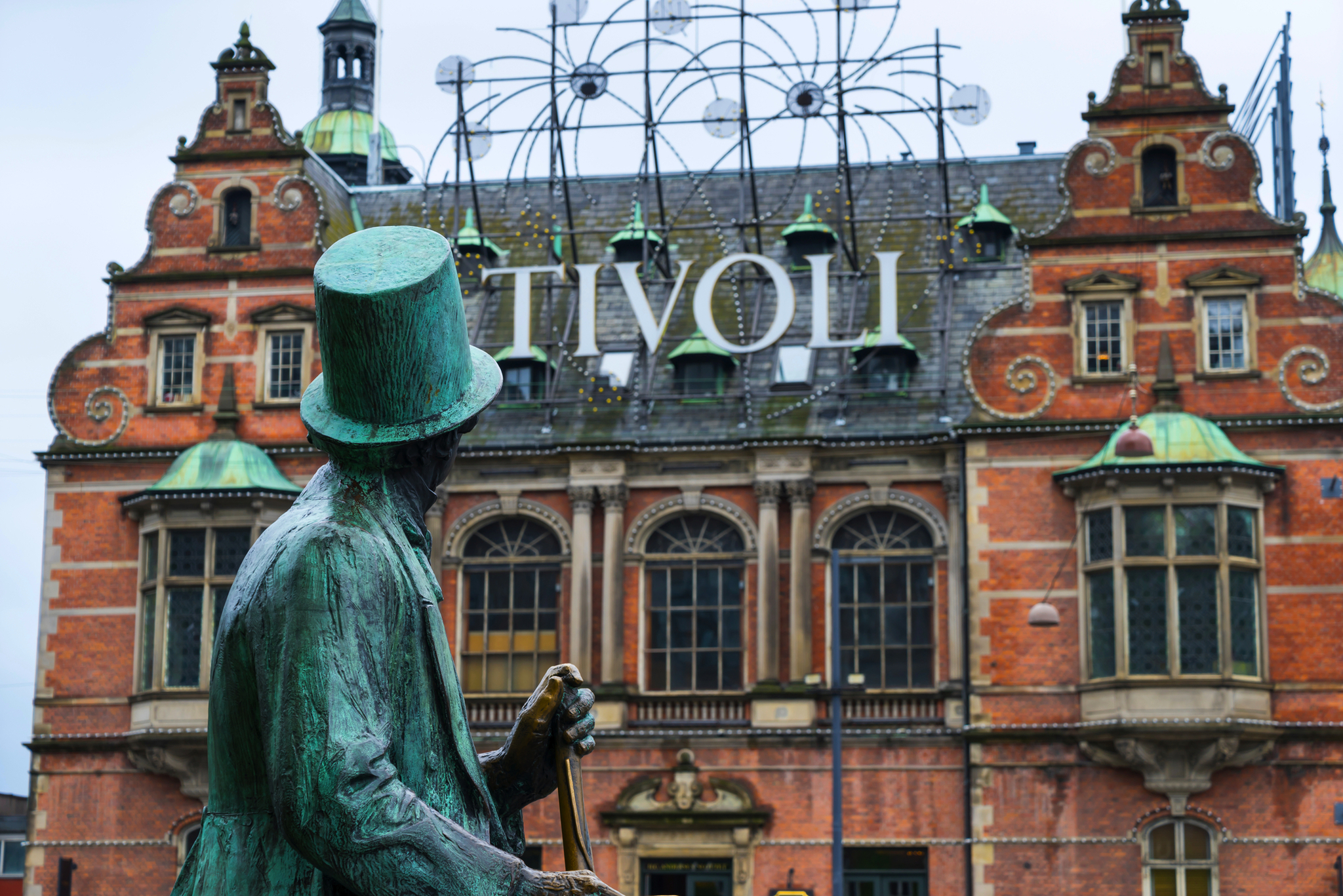 Skulptur im Vordergrund mit Zylinder und Spazierstock, im Hintergrund das markante historische Gebäude des Tivoli Freizeitparks in Kopenhagen, Dänemark.