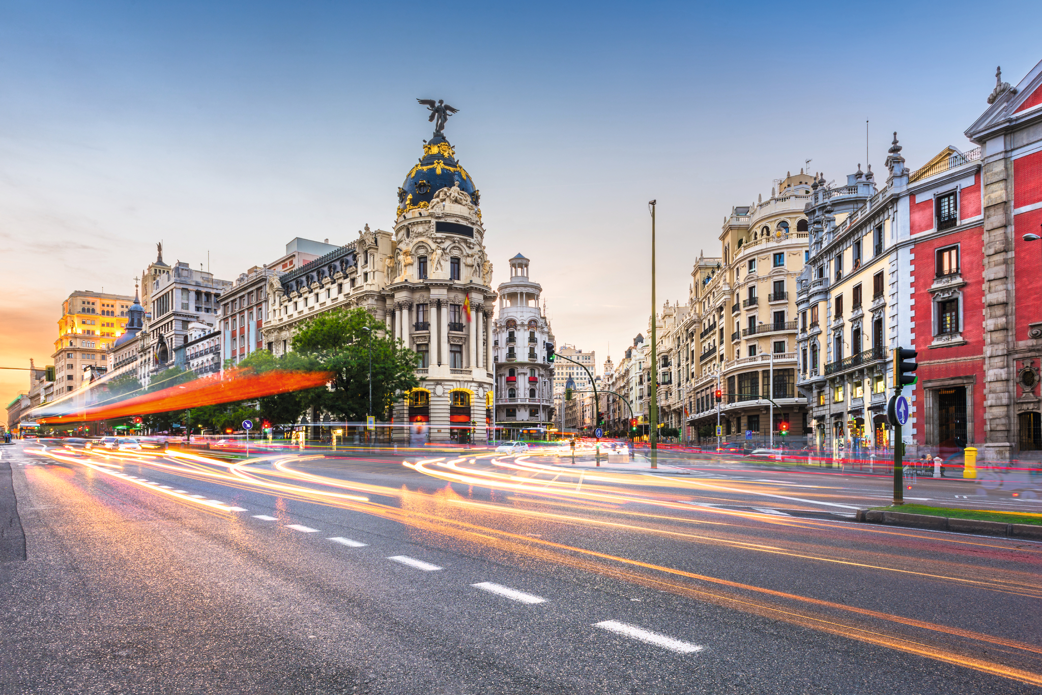 Straßenszene in Madrid bei Sonnenuntergang mit historischen Gebäuden und Lichtspuren.