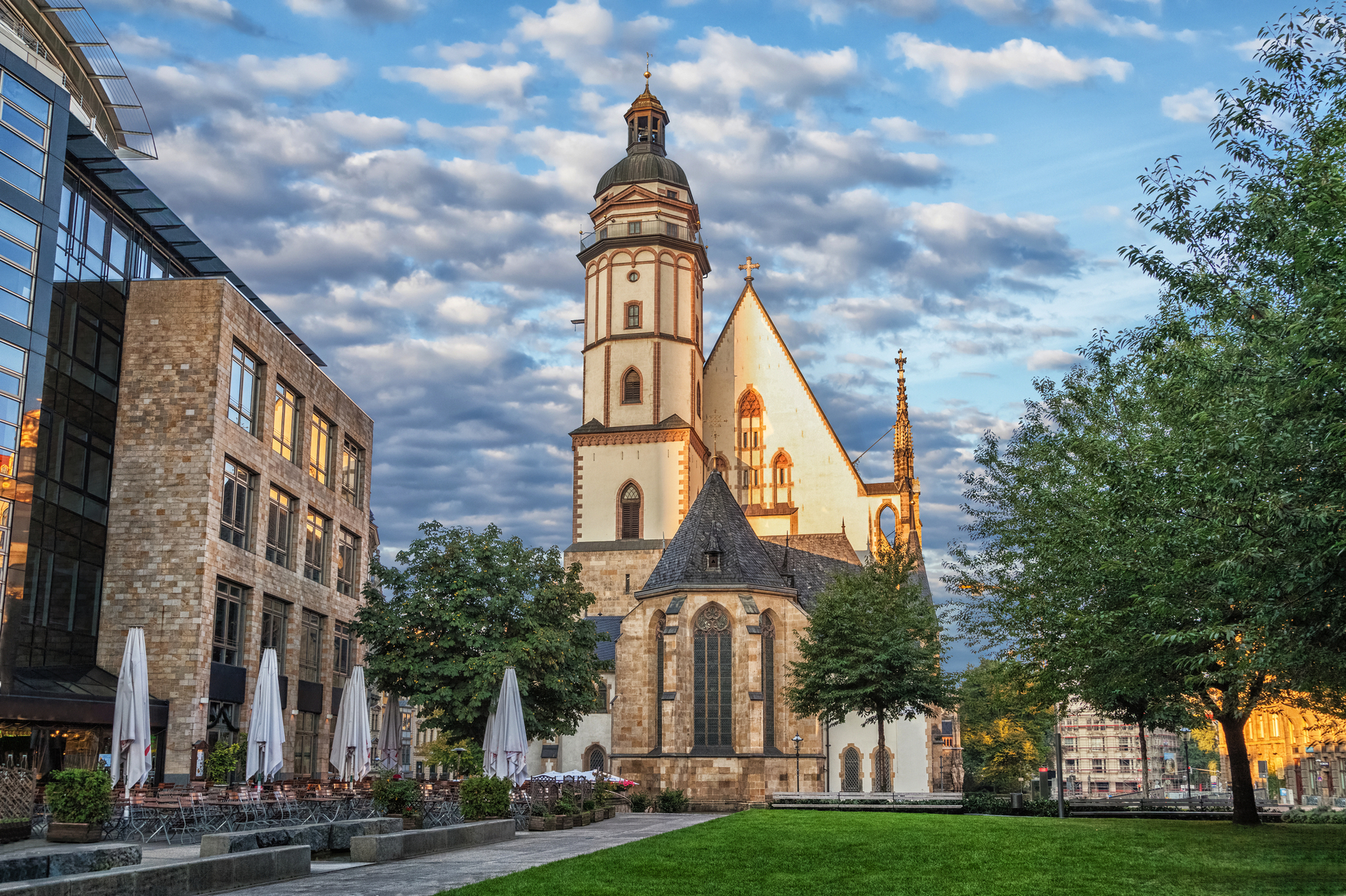 Thomaskirche in Leipzig Kirche mit imposantem Turm neben modernen Gebäuden unter bewölktem Himmel.