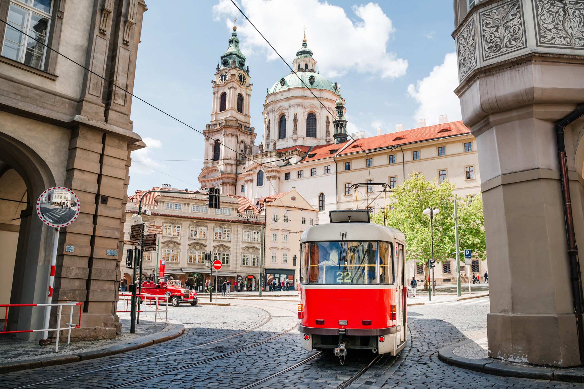 Rote Straßenbahn vor historischer Kirche in einer europäischen Stadt.