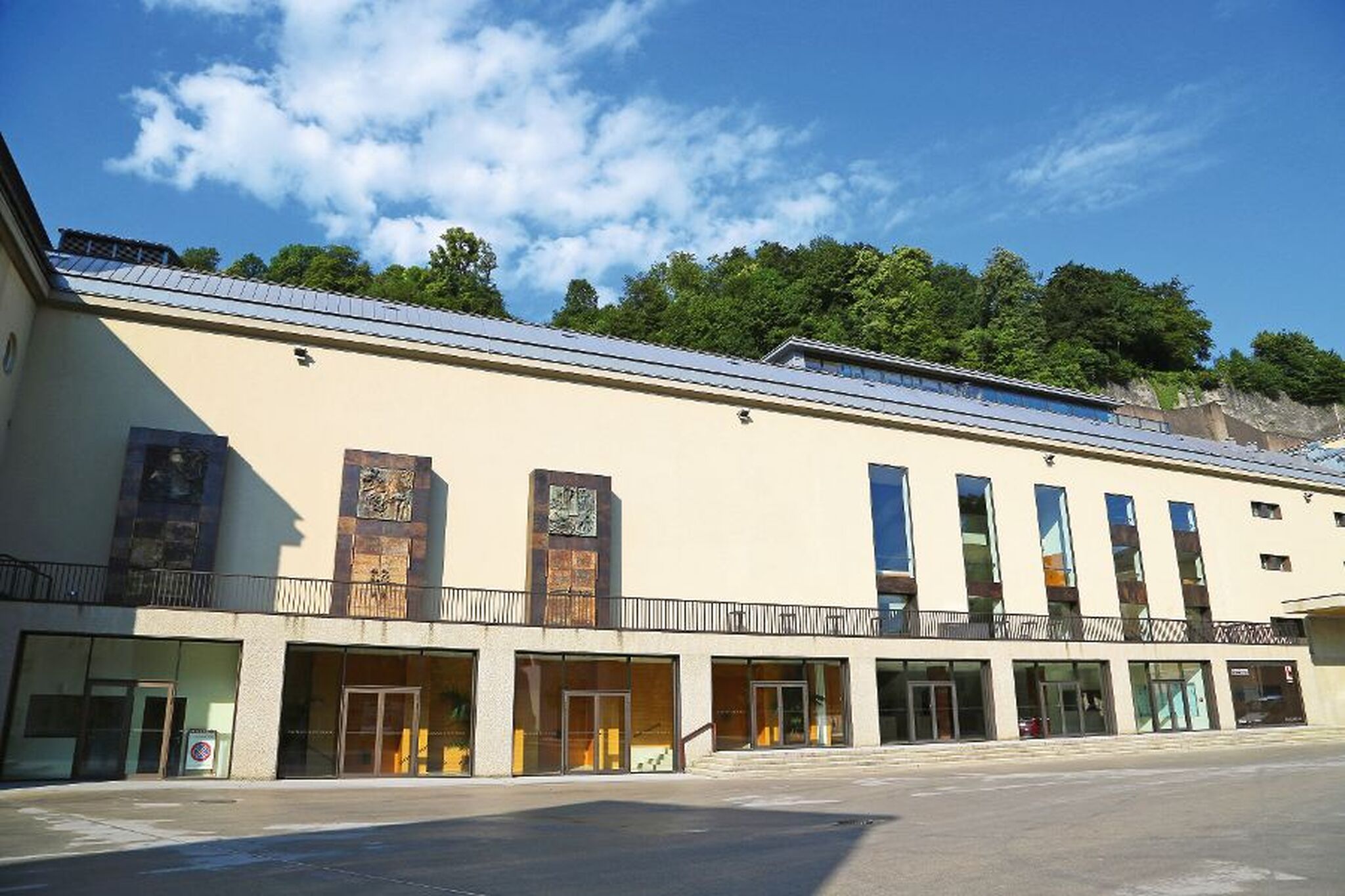Salzburger Festspielhaus Moderne Gebäudeansicht mit großen Fenstern und bewaldetem Hügel im Hintergrund.