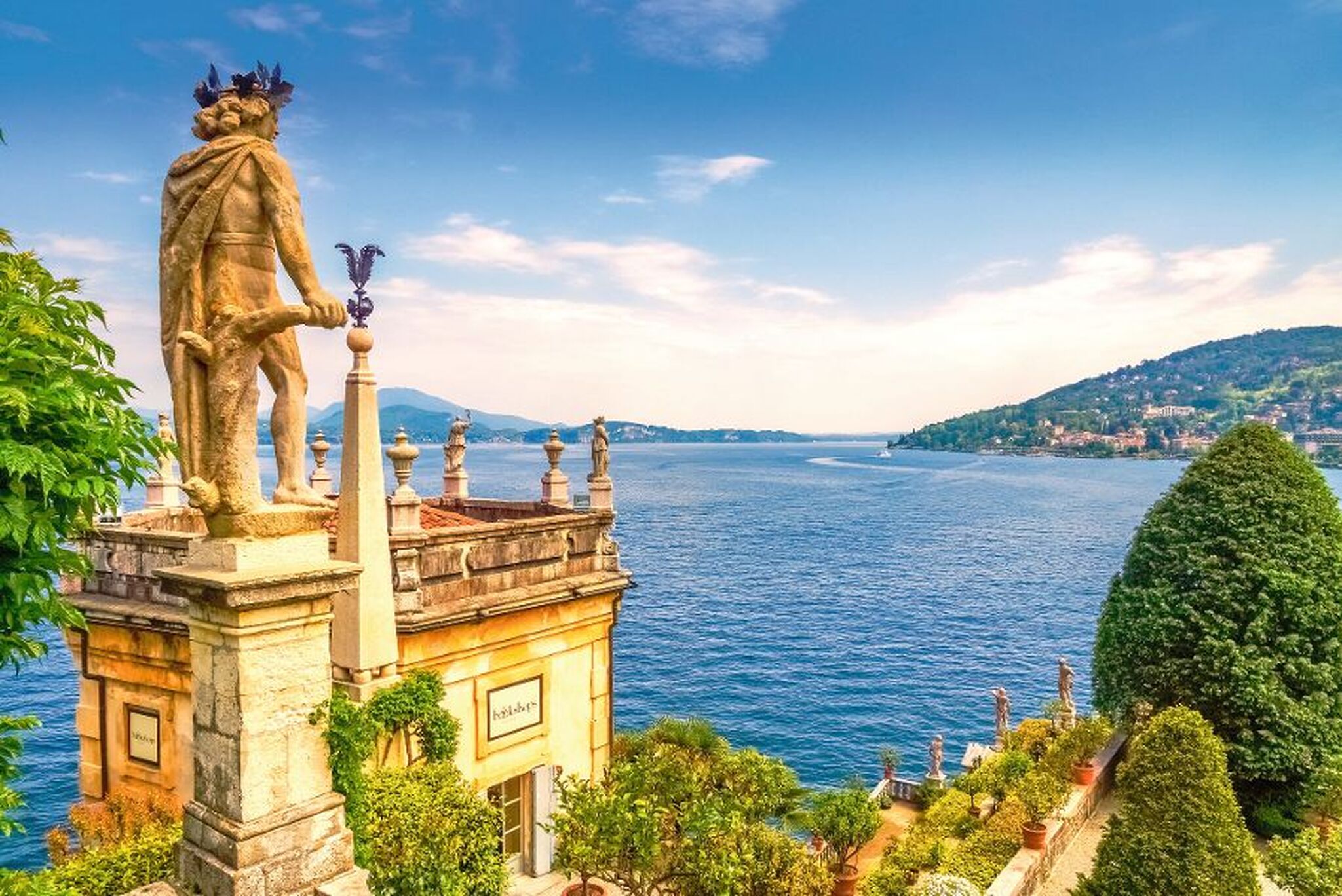 Skulptur mit Blick auf einen See und umliegende Hügel unter blauem Himmel.