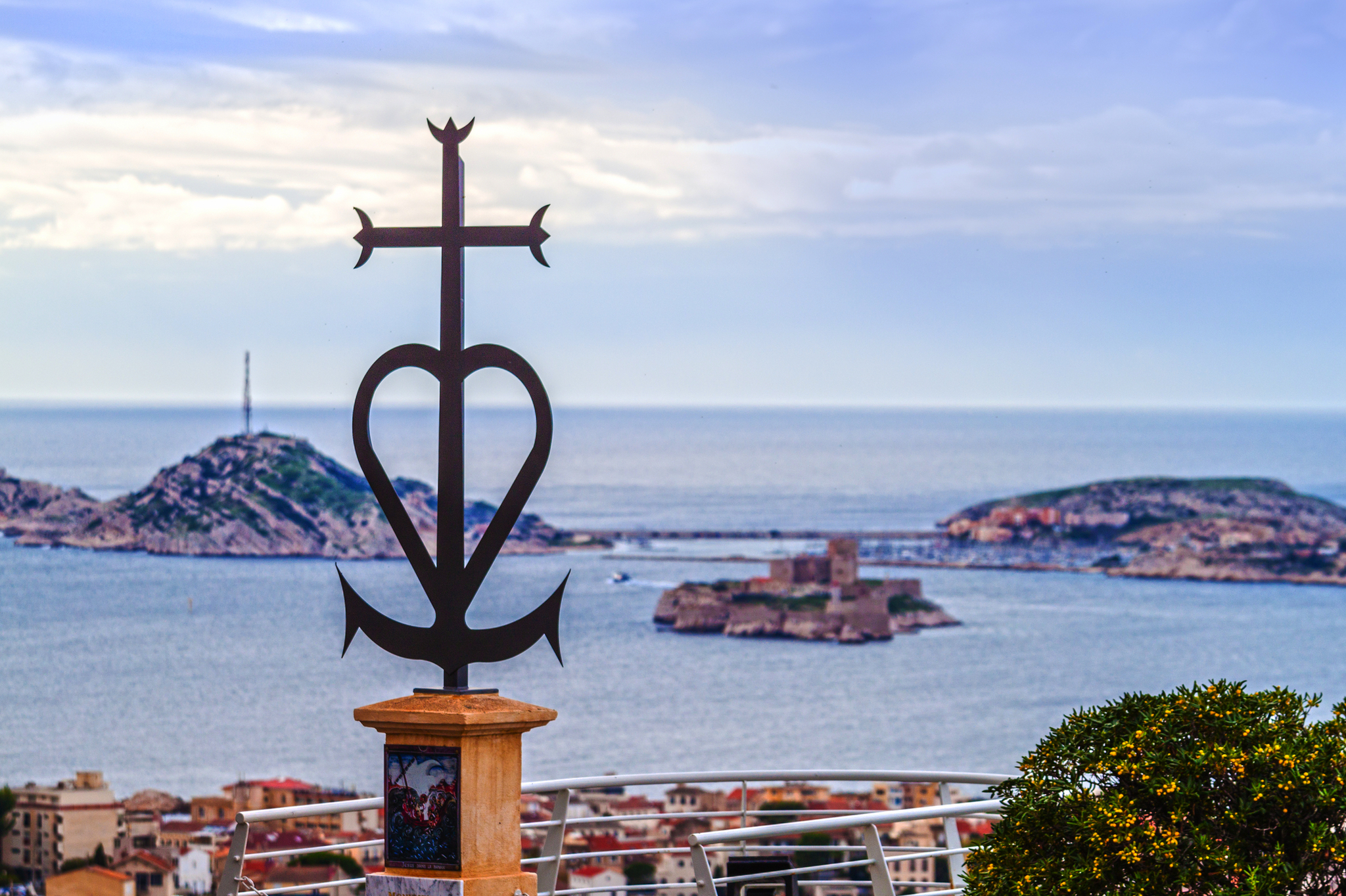 Kunstvolles Kreuz überblickt Stadt am Meer mit Inseln im Hintergrund.