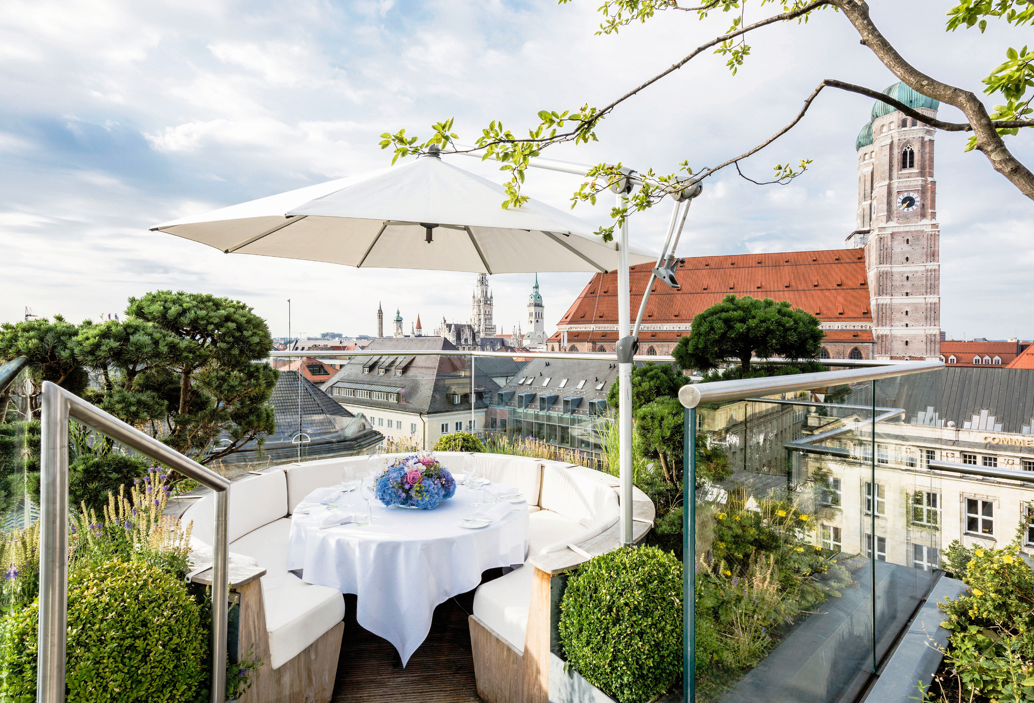 Tisch mit Blumen unter Sonnenschirm auf Terrasse, Ausblick auf Frauenkirche, Hotel Bayerischer Hof.