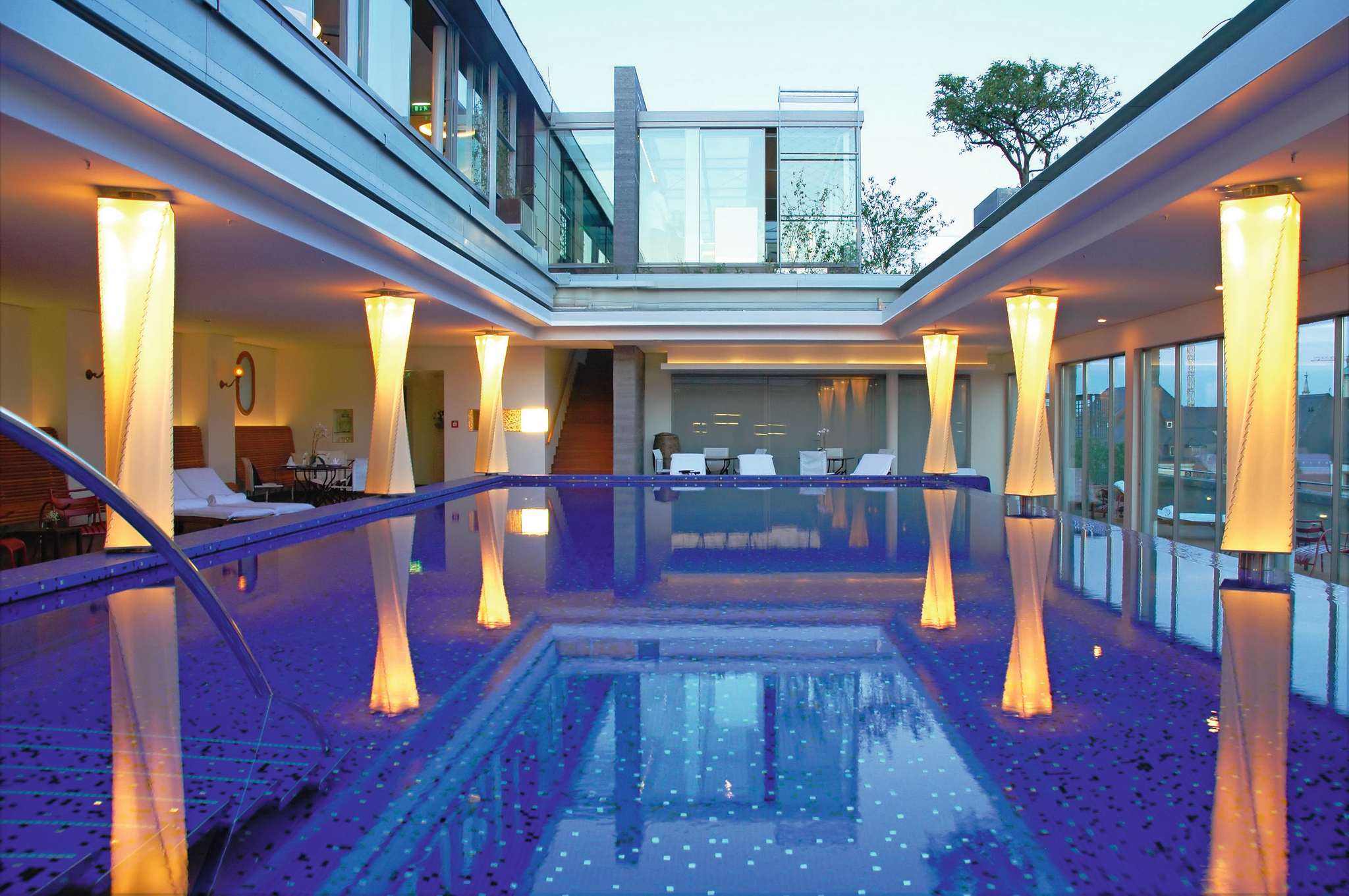 Hotelpool im Innenhof mit beleuchteten Säulen, umgeben von Glaswänden.
