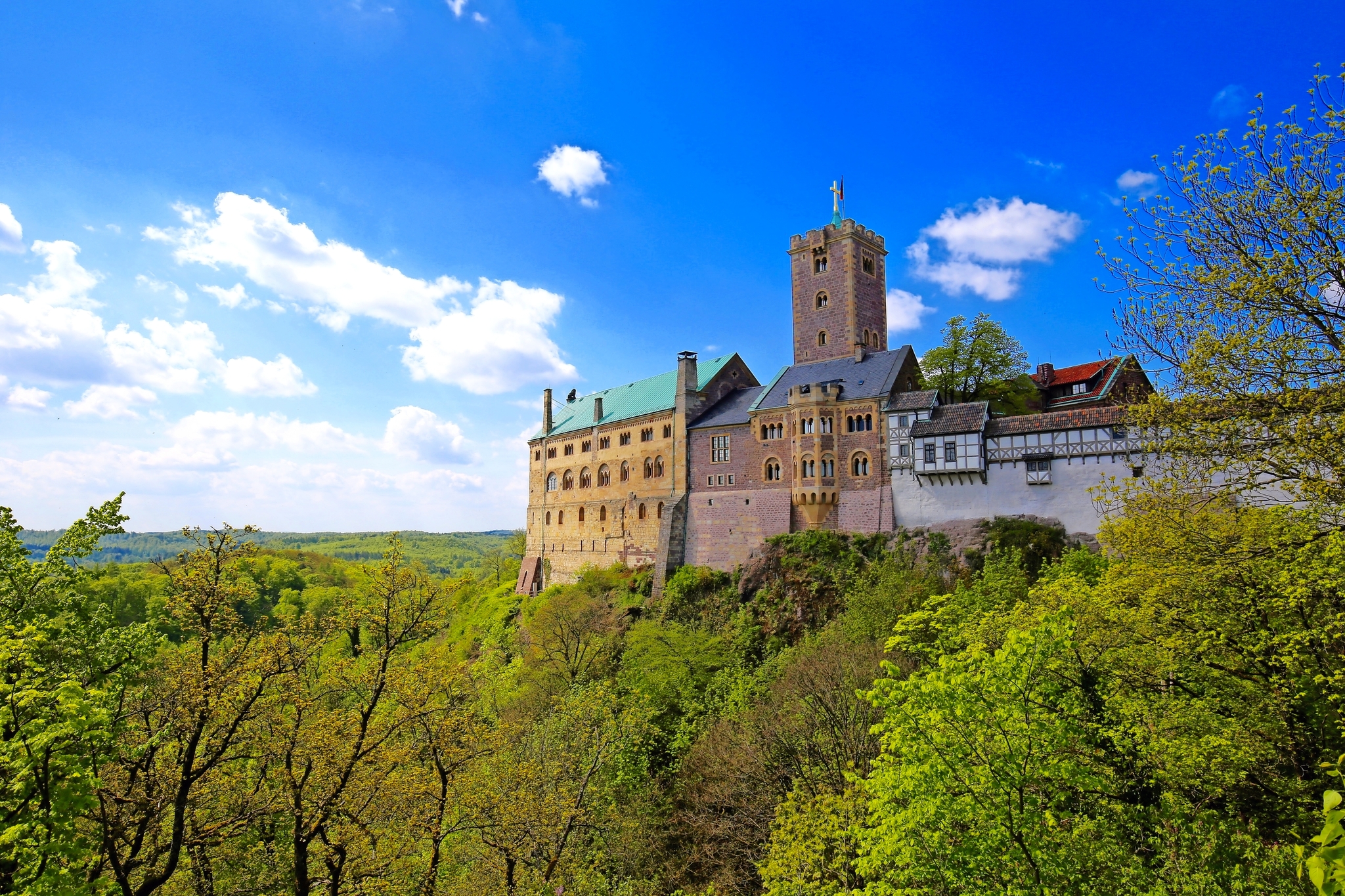 Ein historisches Schloss auf einem grünen Hügel unter blauem Himmel mit Wolken.