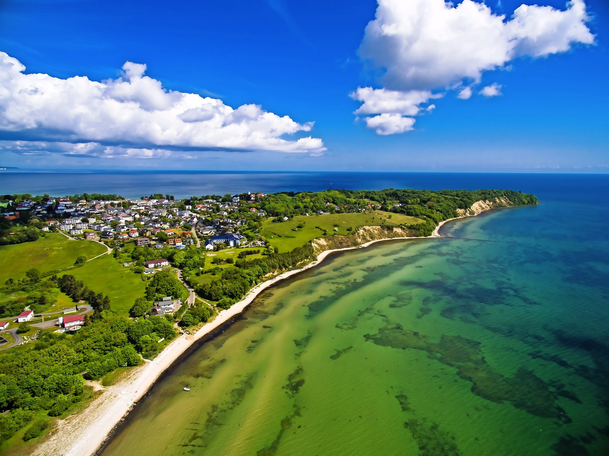 Luftaufnahme einer Küstenlandschaft mit Häusern, Strand und bewölktem Himmel.