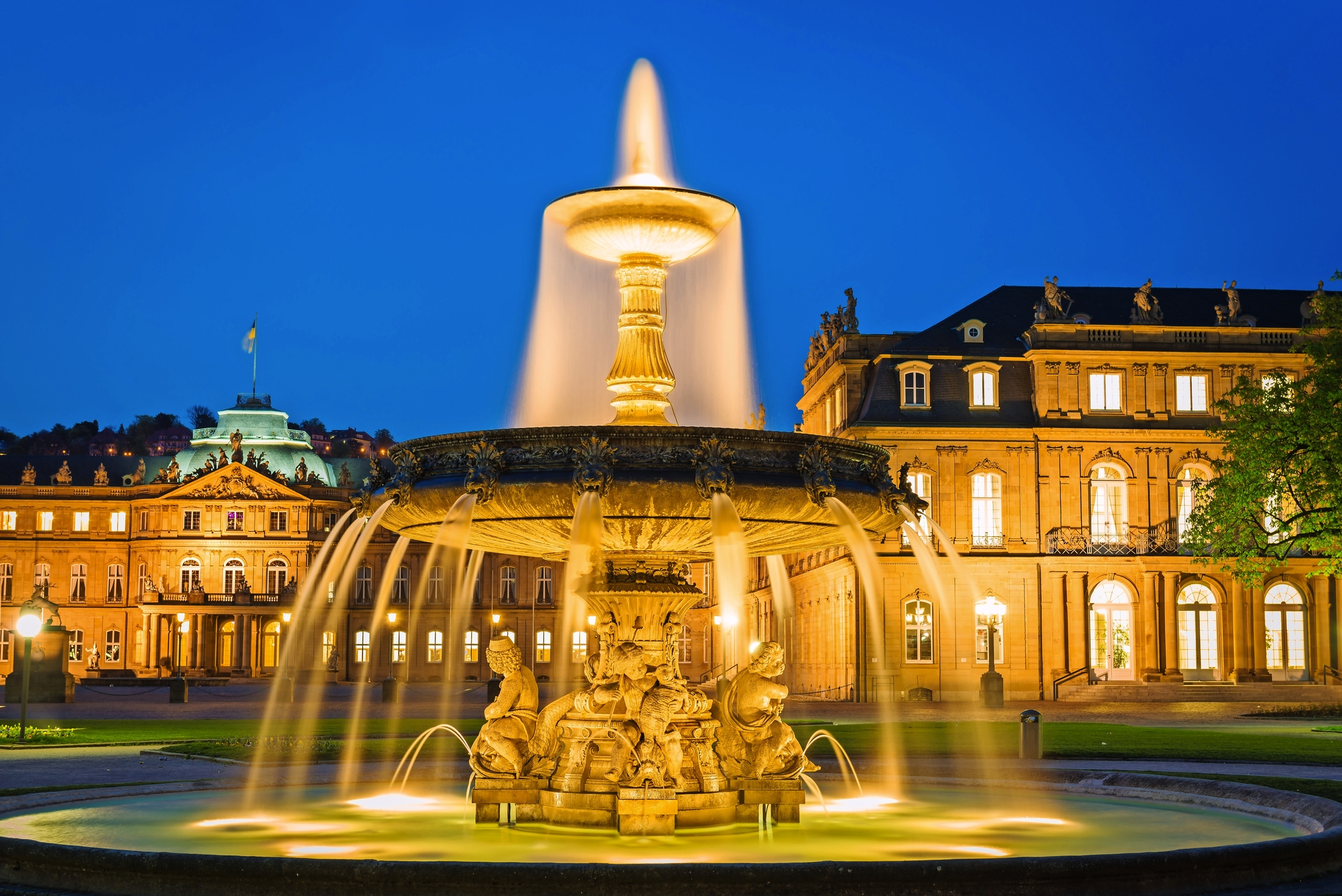 Beleuchteter Brunnen vor historischer Architektur bei Nacht.
