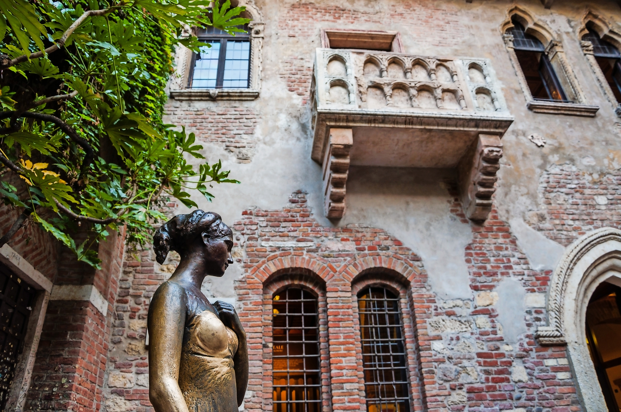 der berühmte Balkon von Shakespeares "Romeo und Julia" in Verona, Italien Bronzestatue einer Frau in einem Innenhof vor einer alten Backsteinfassade mit einem kleinen Balkon darüber.