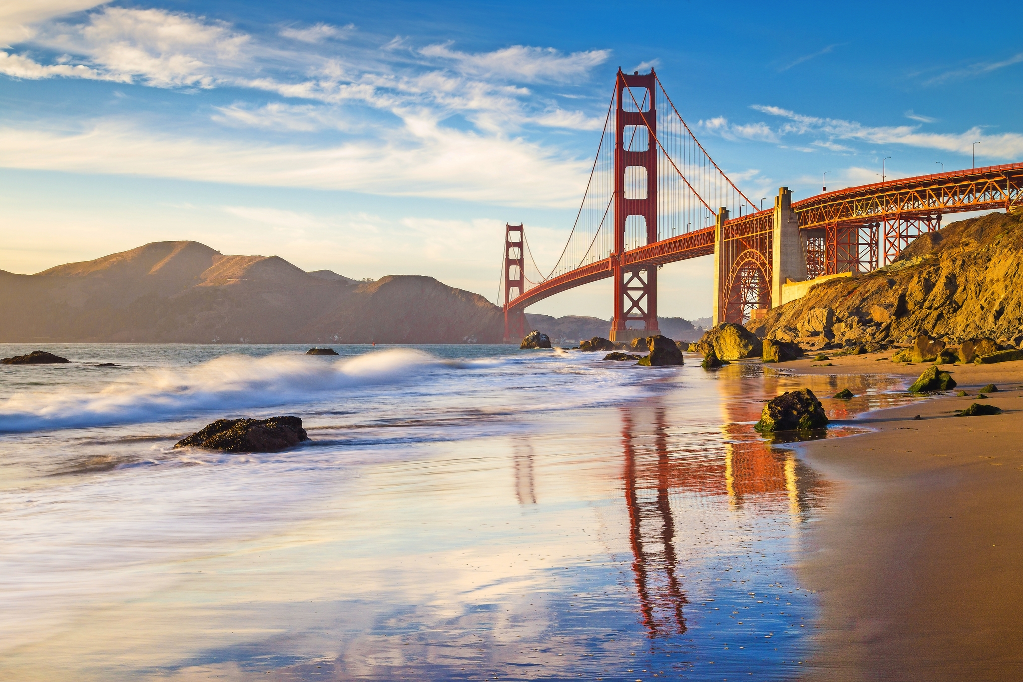 Golden Gate Bridge bei Sonnenuntergang mit Strand und Wellen im Vordergrund.